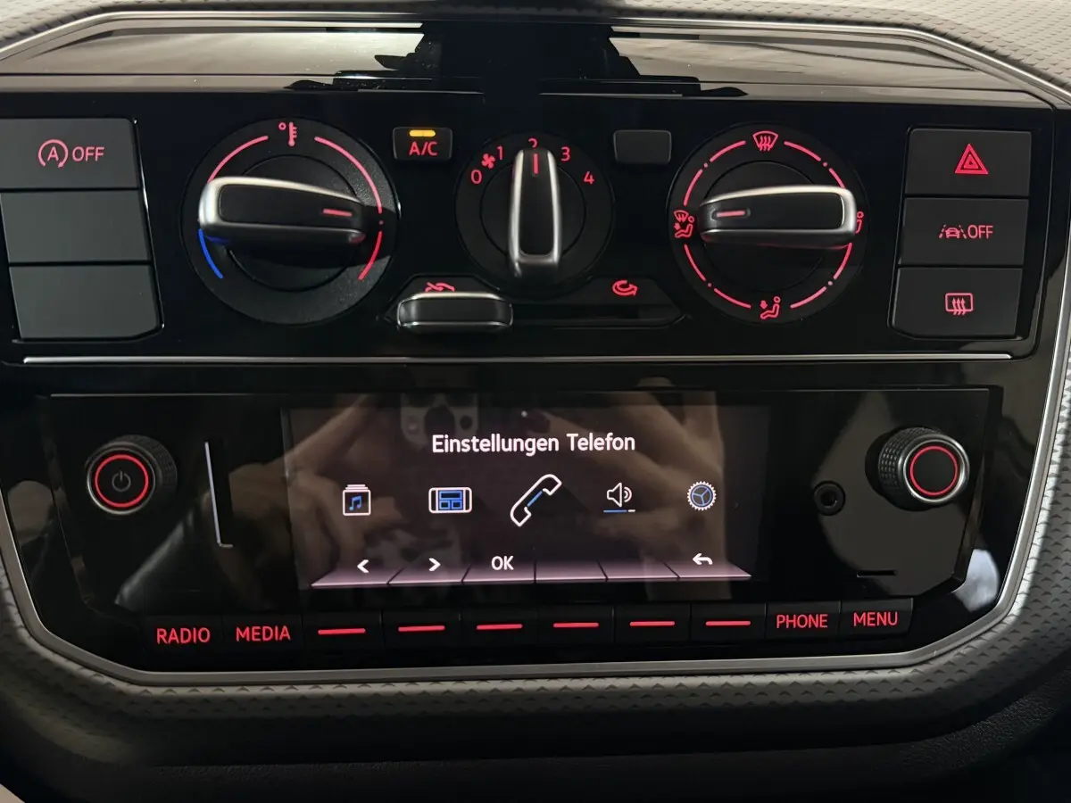 Tableau de bord noir du Volkswagen Up 2022 avec commandes de climatisation et écran tactile central allumé.