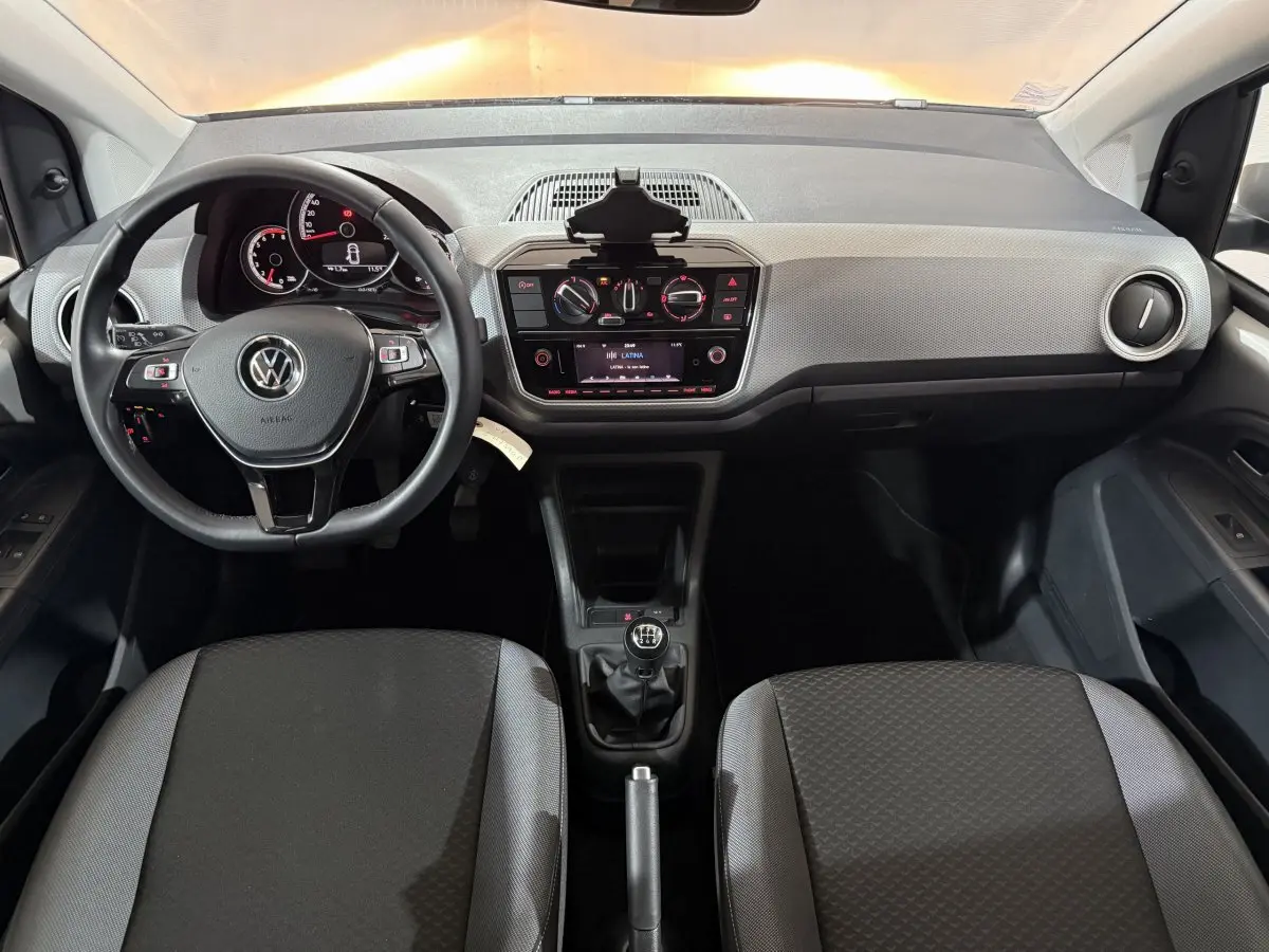 Vue intérieure frontale du tableau de bord gris clair et noir de la Volkswagen Up 1.0 65 Active avec volant cuir et boîte manuelle.