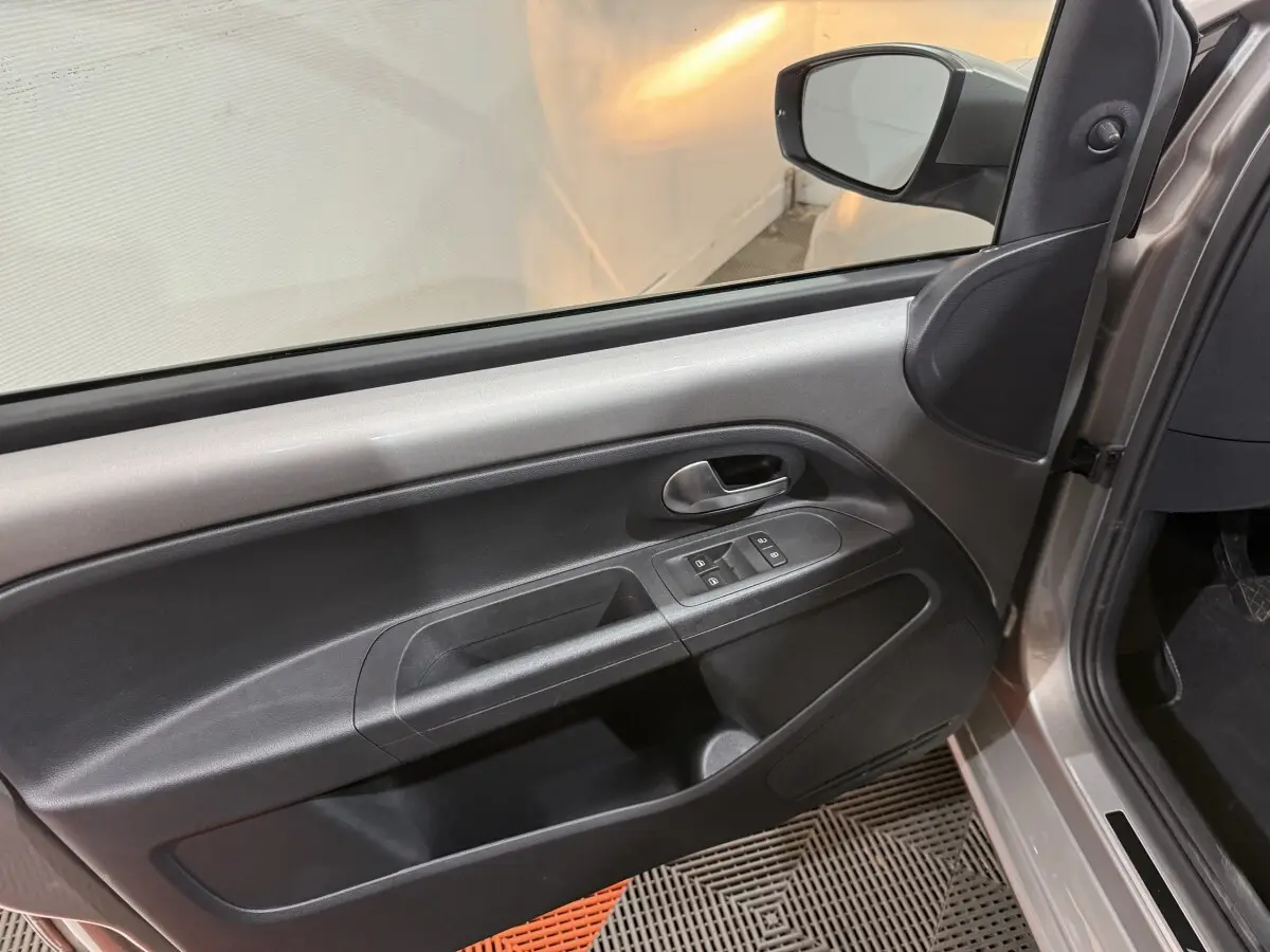 Vue intérieure du panneau de porte avant gauche gris foncé de la Volkswagen Up 1.0 65 Active avec commandes des vitres et poignée métallique.