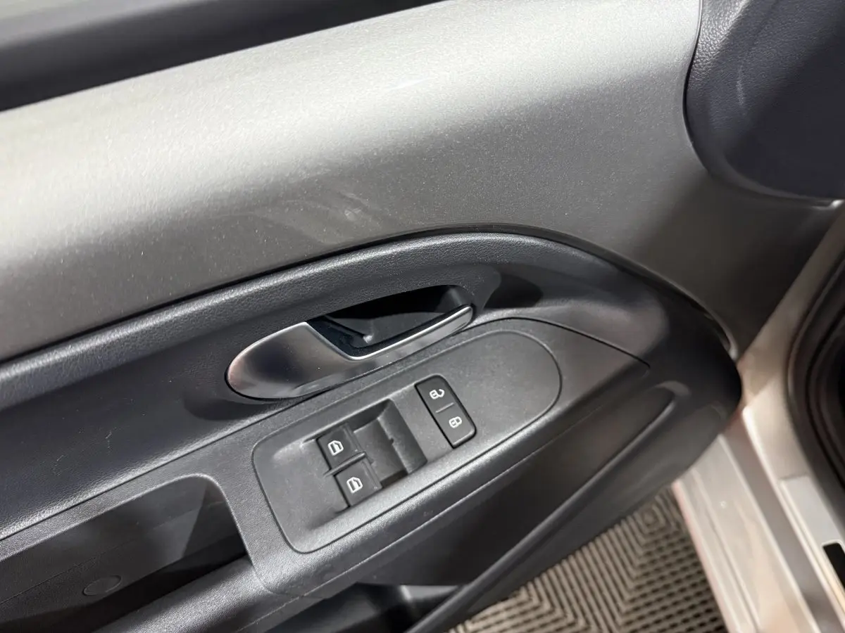 Gros plan sur la commande des vitres et la poignée intérieure côté conducteur d’une Volkswagen Up gris foncé.