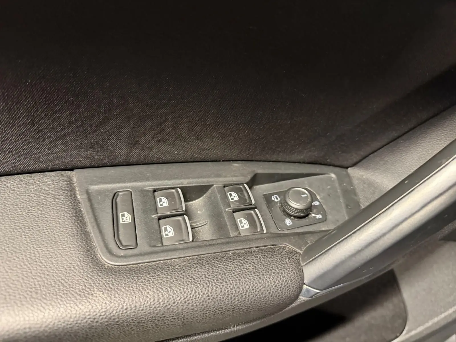 Gros plan sur les commandes des vitres électriques et rétroviseurs rabattables côté gauche d’un Volkswagen Tiguan gris.