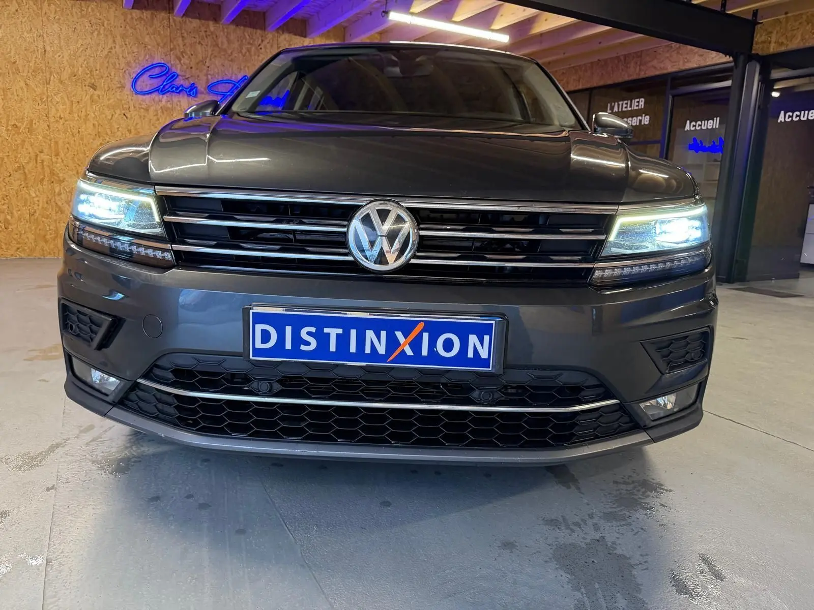 Vue frontale d'un Volkswagen Tiguan gris avec phares allumés et plaque Distinxion visible en intérieur.