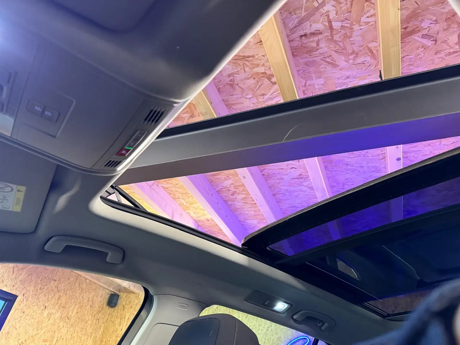 Vue intérieure du toit ouvrant panoramique ouvert du Volkswagen Tiguan gris, avec éclairage intérieur et plafond en bois visible.