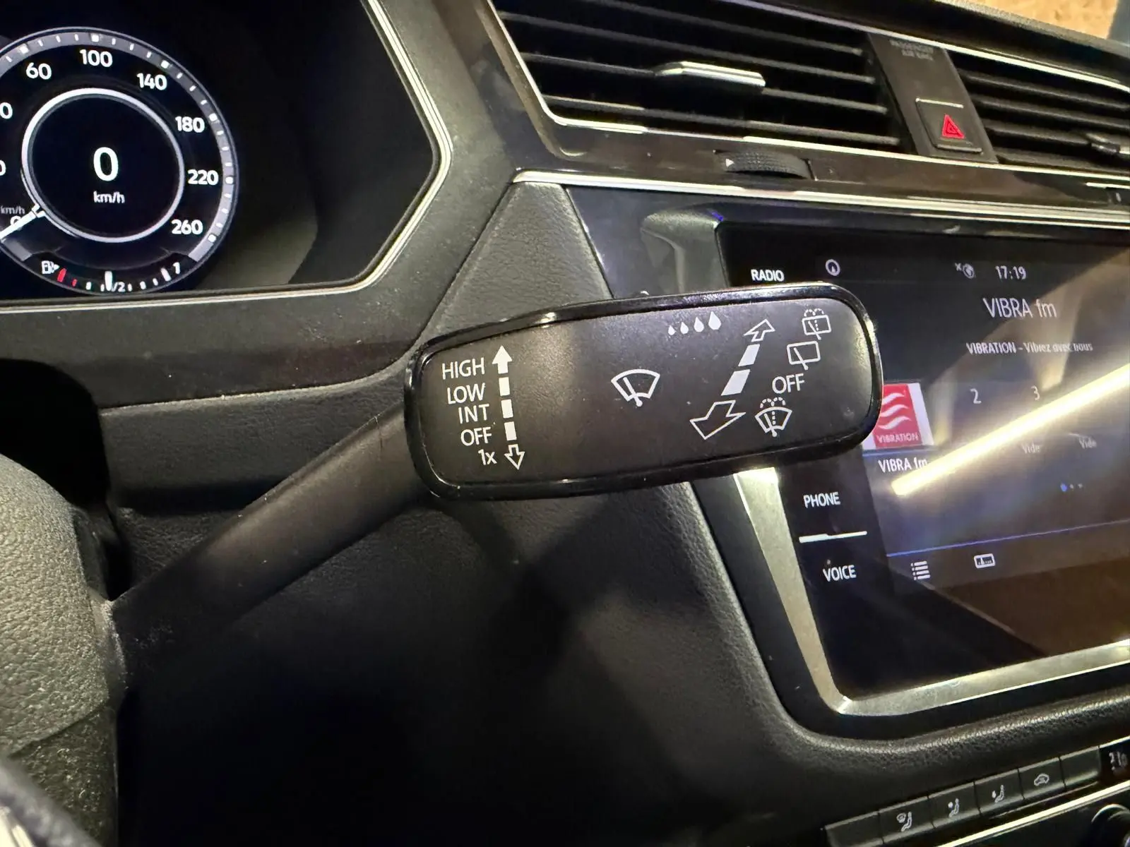 Gros plan sur la commande d'essuie-glace du Volkswagen Tiguan gris, avec tableau de bord numérique et écran tactile visible.