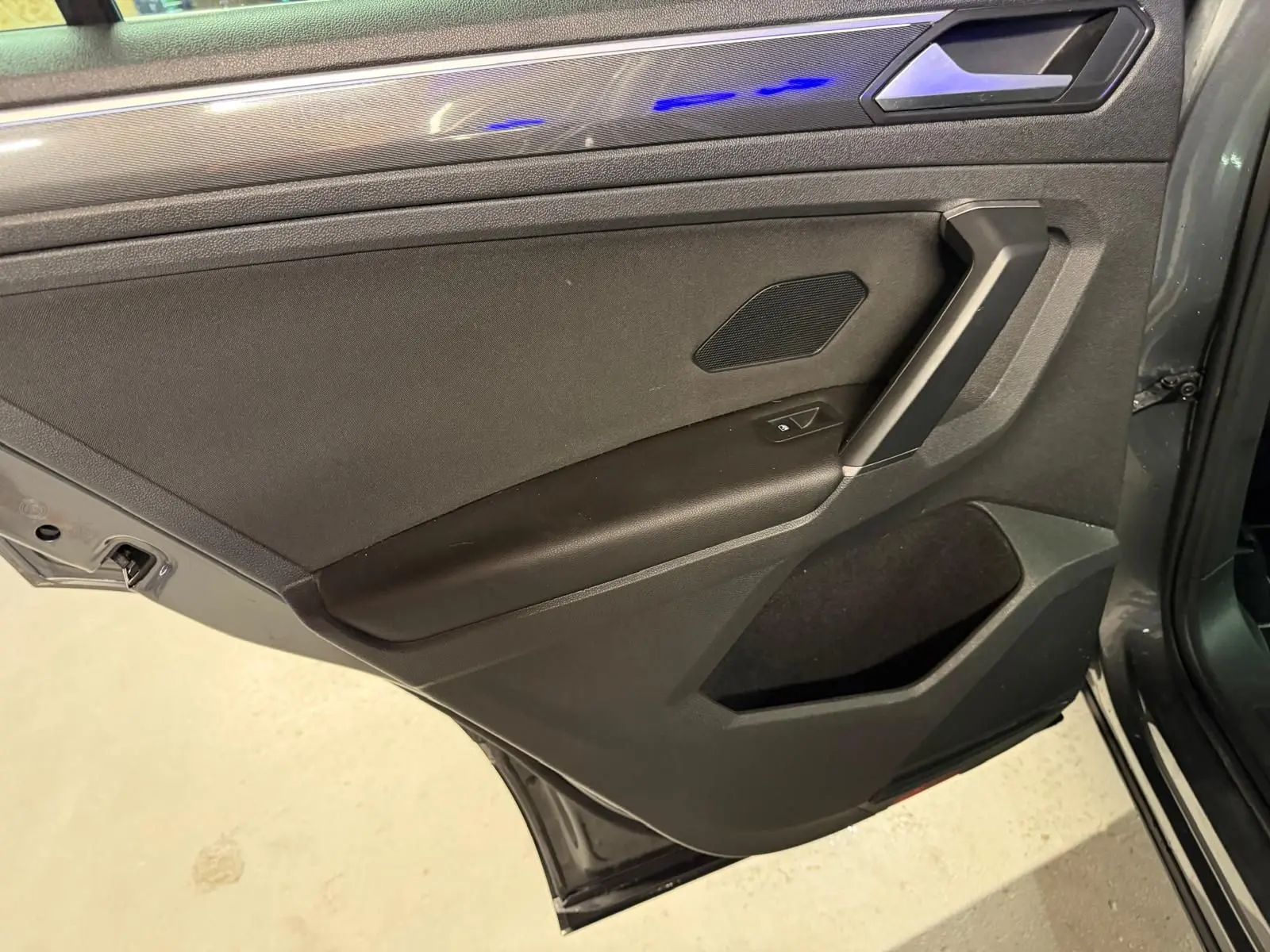 Vue intérieure de la porte arrière droite gris tungstène du Volkswagen Tiguan 2018 avec éclairage d'ambiance bleu.