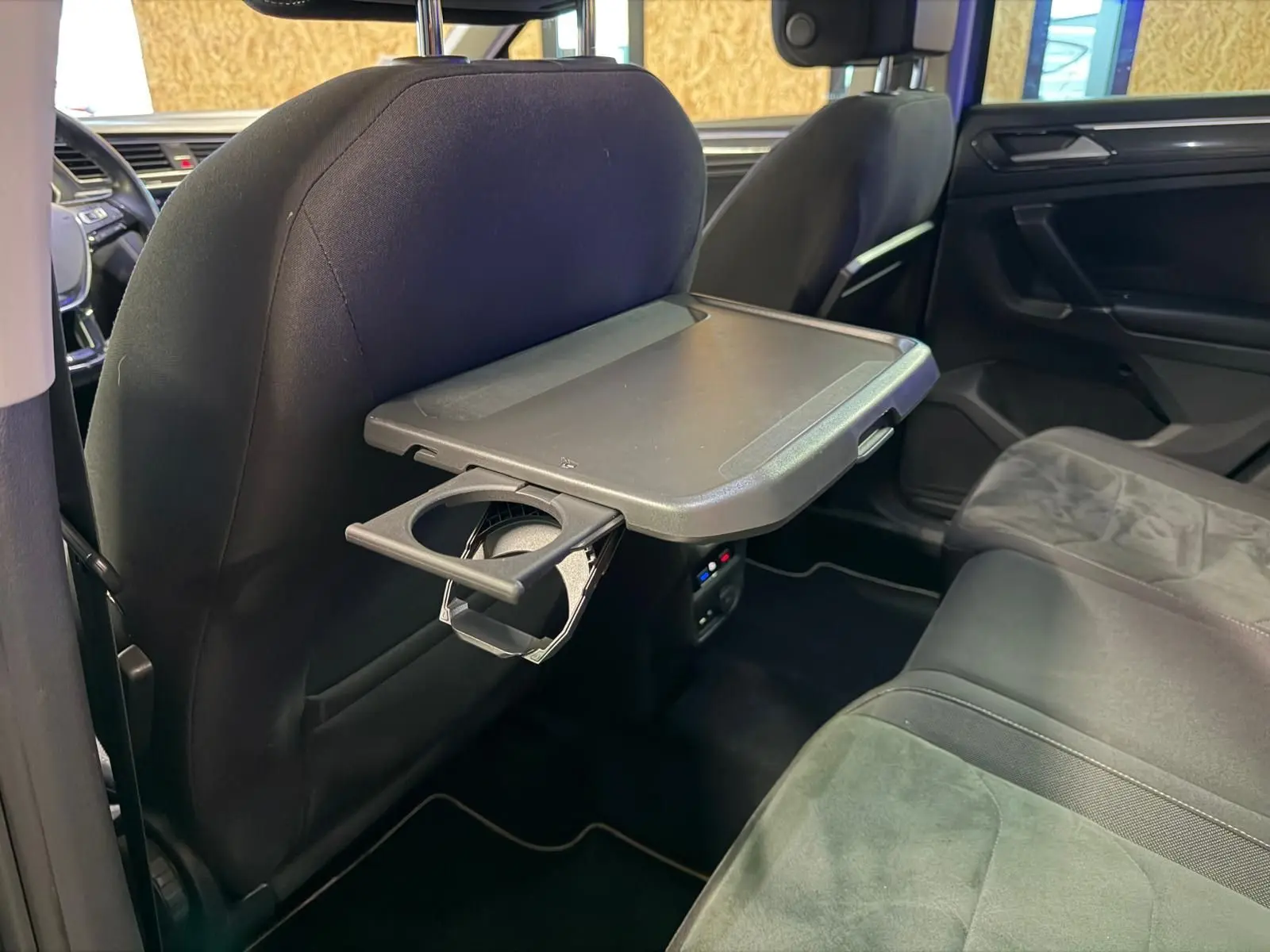 Intérieur arrière du Volkswagen Tiguan gris, vue côté droit avec tablette rabattable et porte-gobelet sur siège avant.