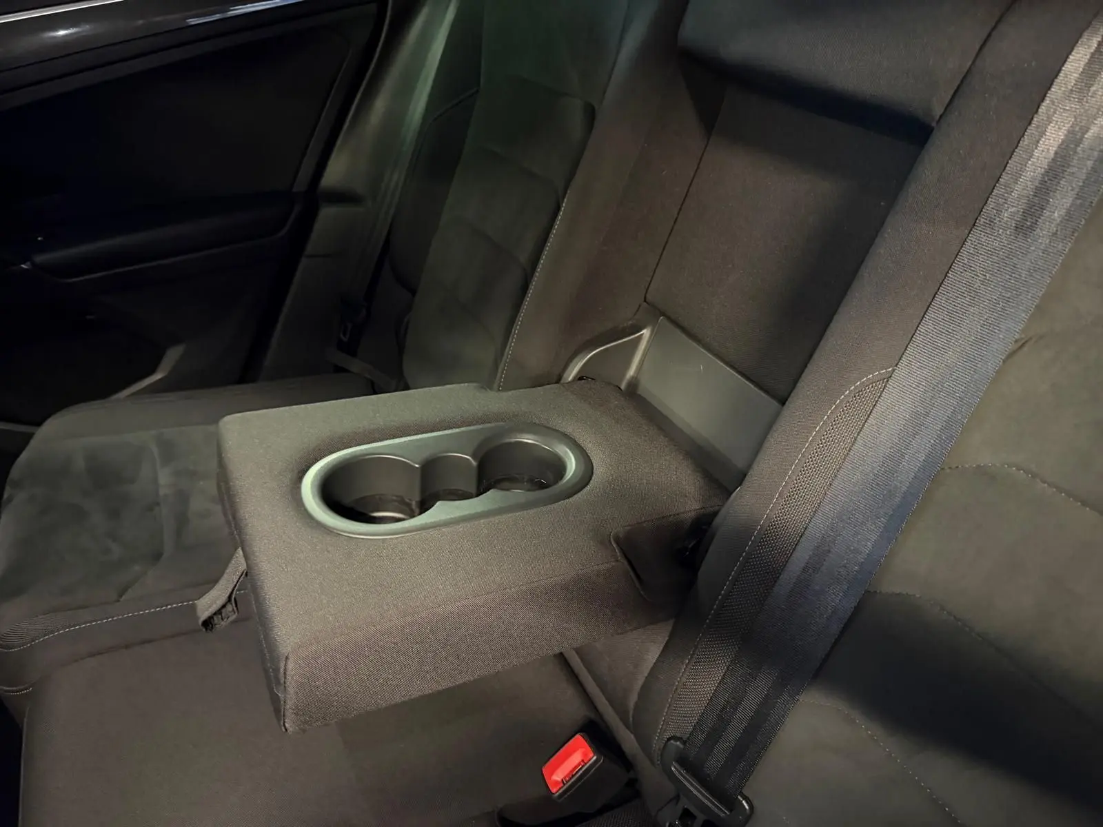 Vue rapprochée de l'accoudoir central arrière avec porte-gobelets du Volkswagen Tiguan gris, banquette arrière en tissu noir.