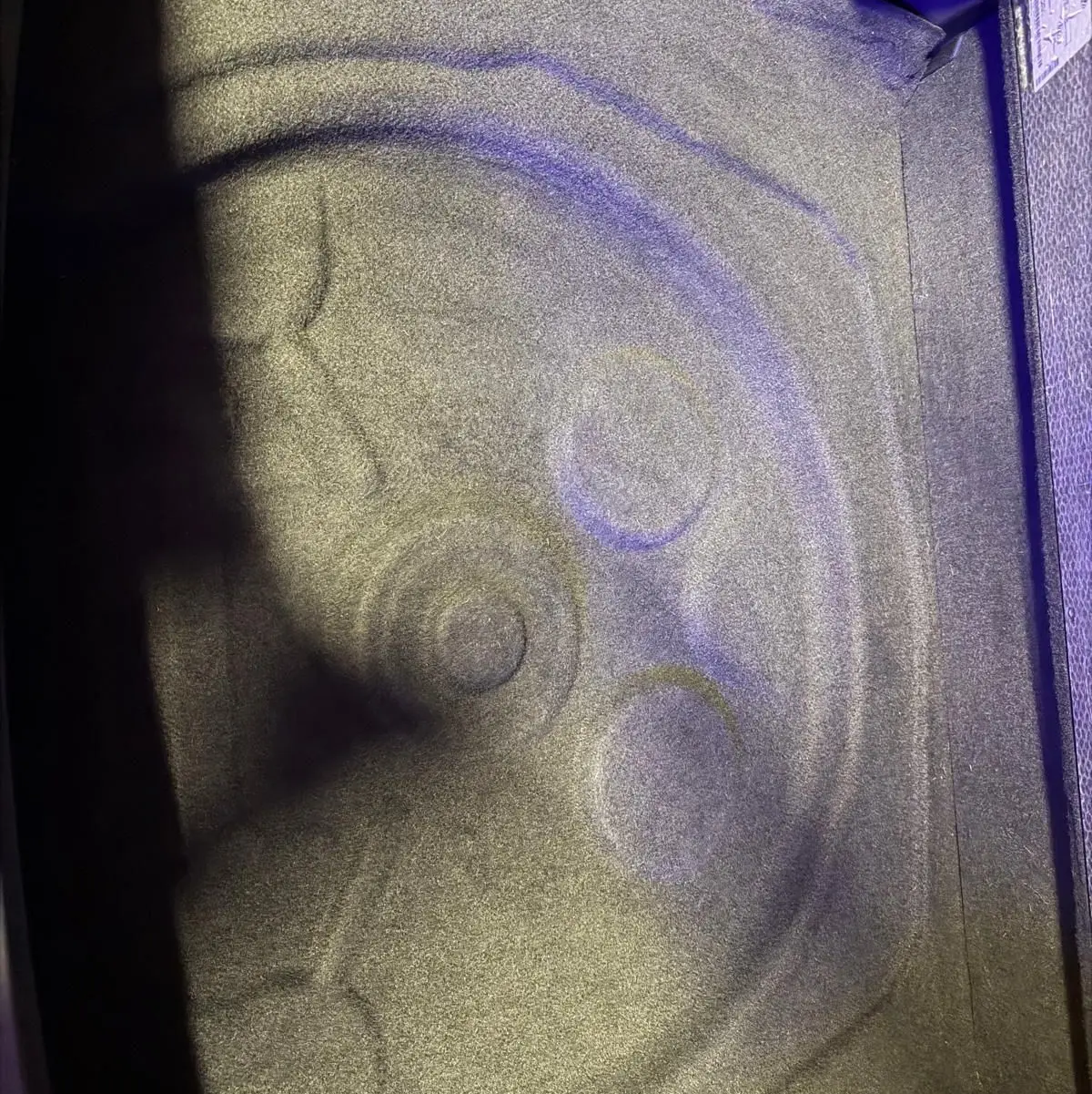 Gros plan sur le compartiment de roue de secours du coffre d’un Volkswagen Tiguan gris, intérieur vide et propre.