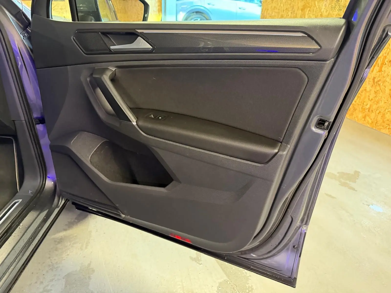 Vue intérieure côté gauche de la porte avant d'un Volkswagen Tiguan gris, avec garniture noire et poignée intégrée.