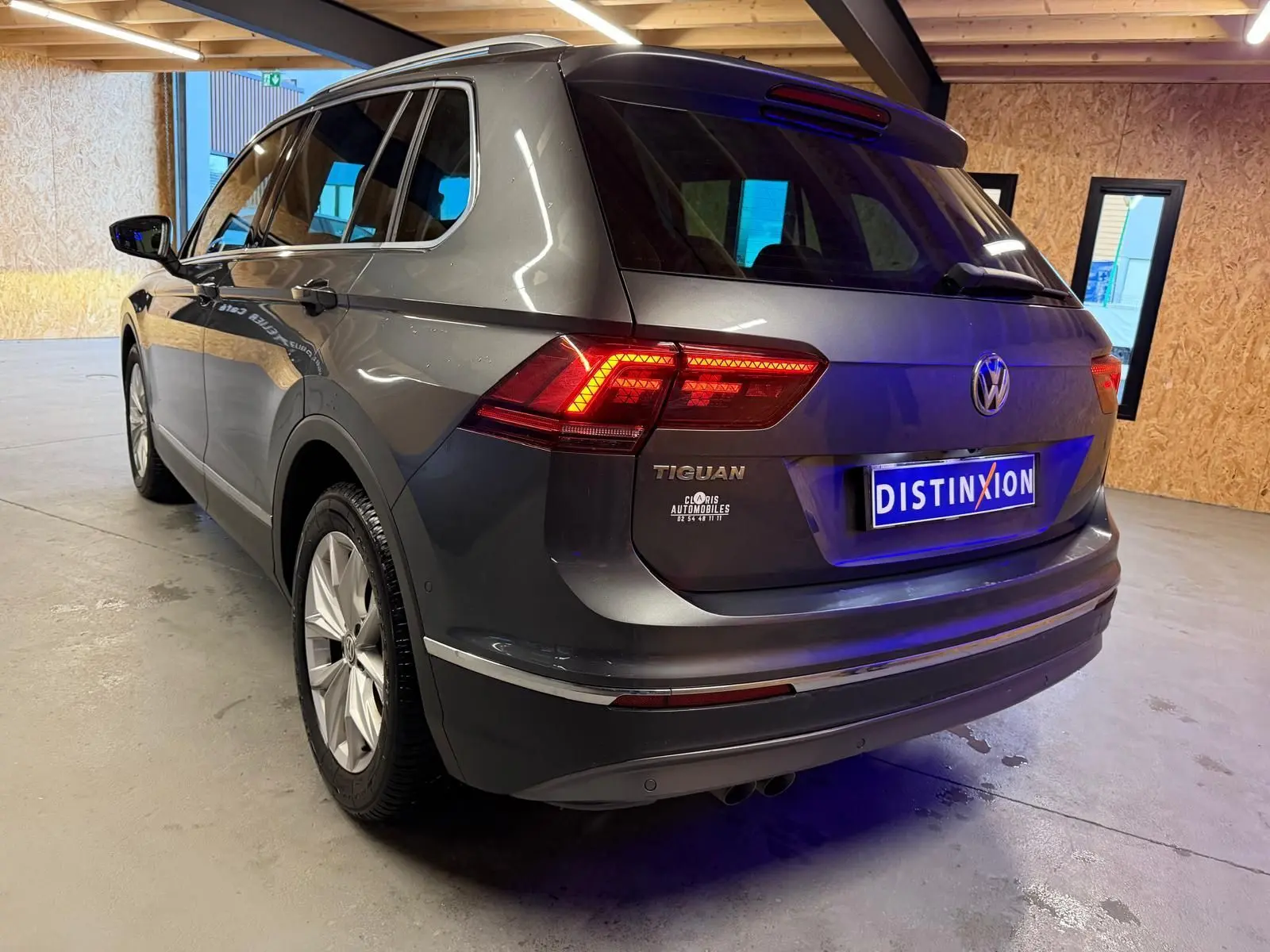 Vue 3/4 arrière droite d'un Volkswagen Tiguan gris avec feux arrière allumés dans un garage.