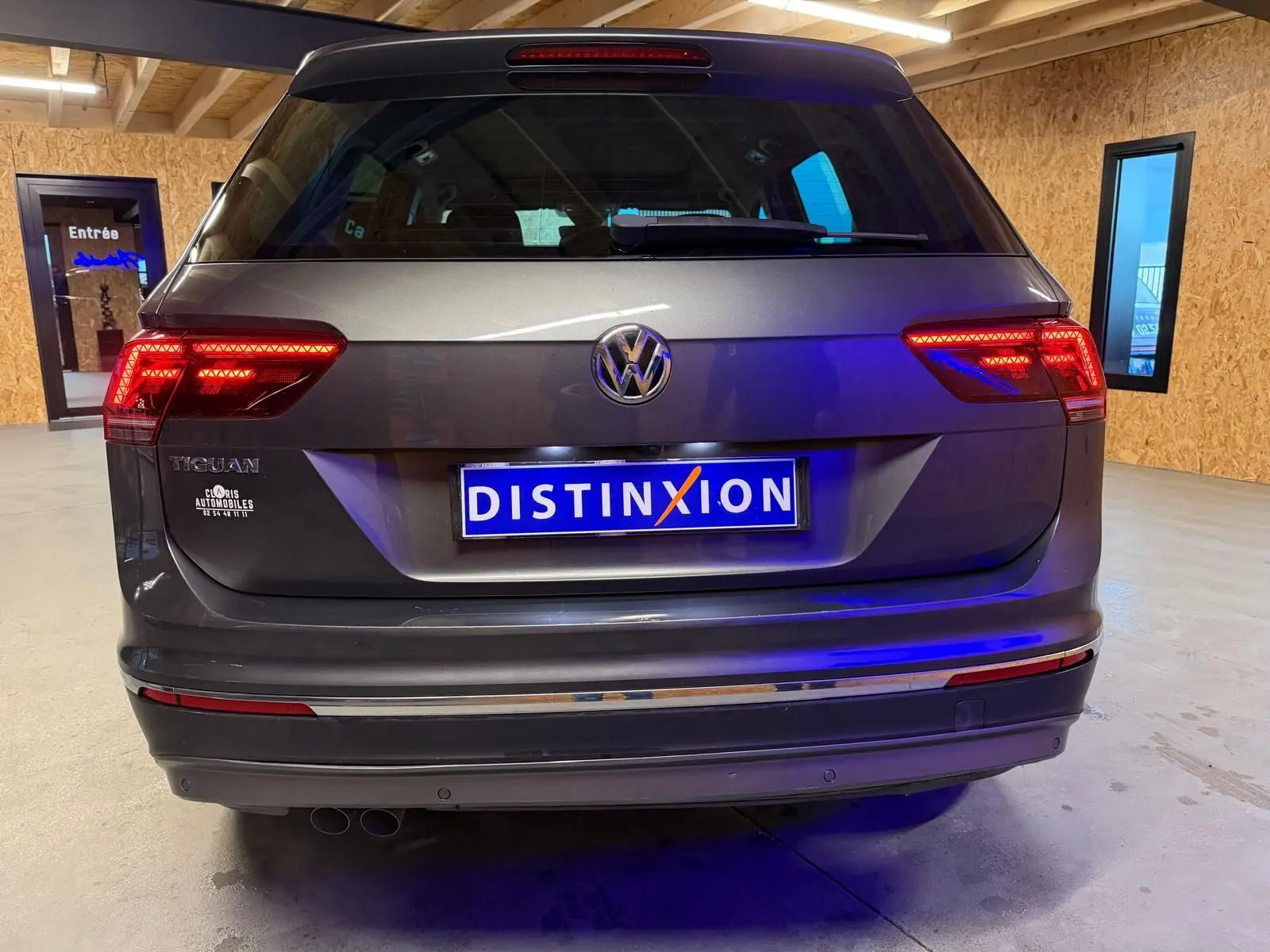 Vue arrière d'un Volkswagen Tiguan gris avec feux allumés dans un garage en bois.