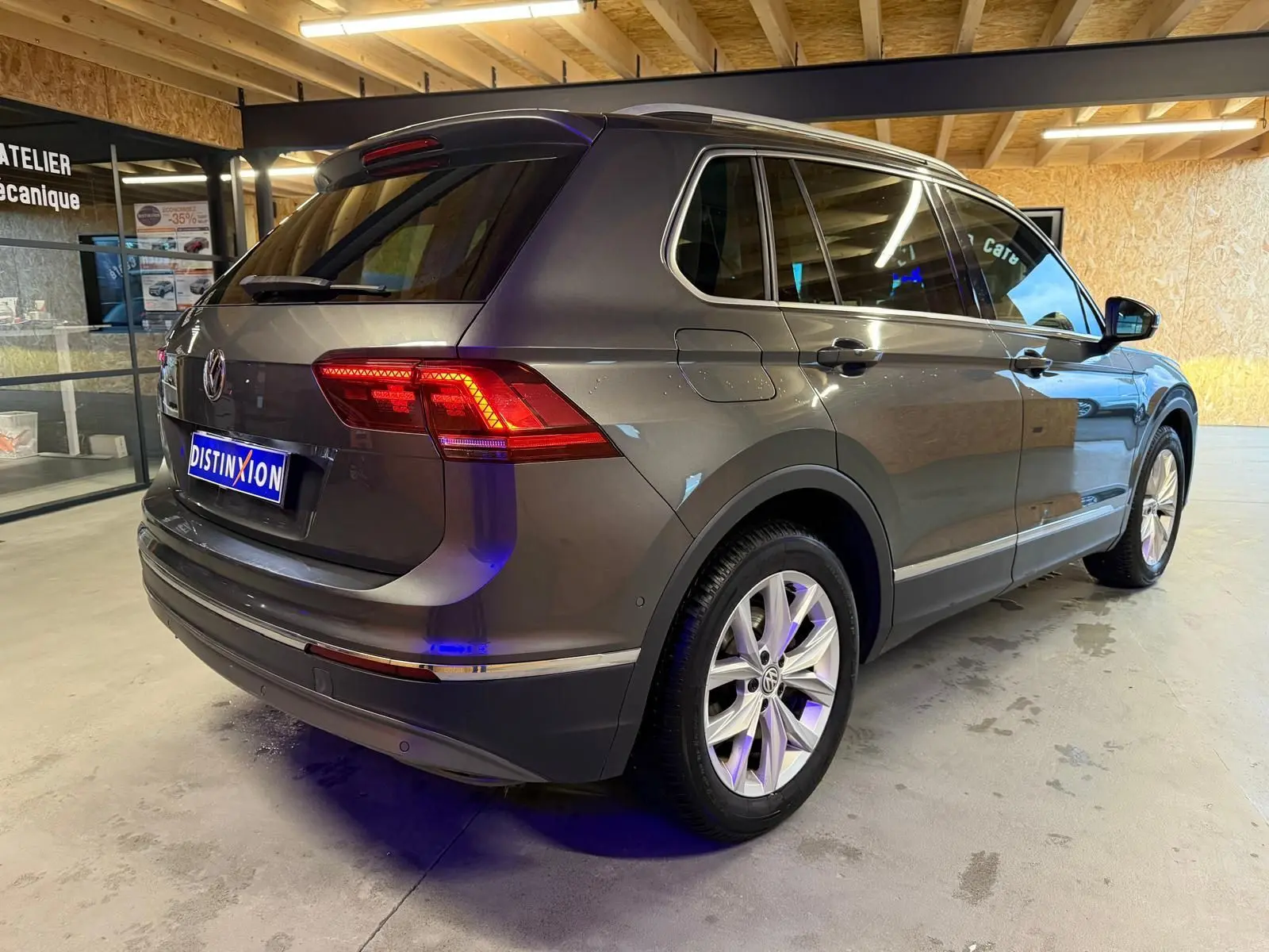 Volkswagen Tiguan gris 3/4 arrière droit en intérieur, avec jantes alu et vitres teintées.