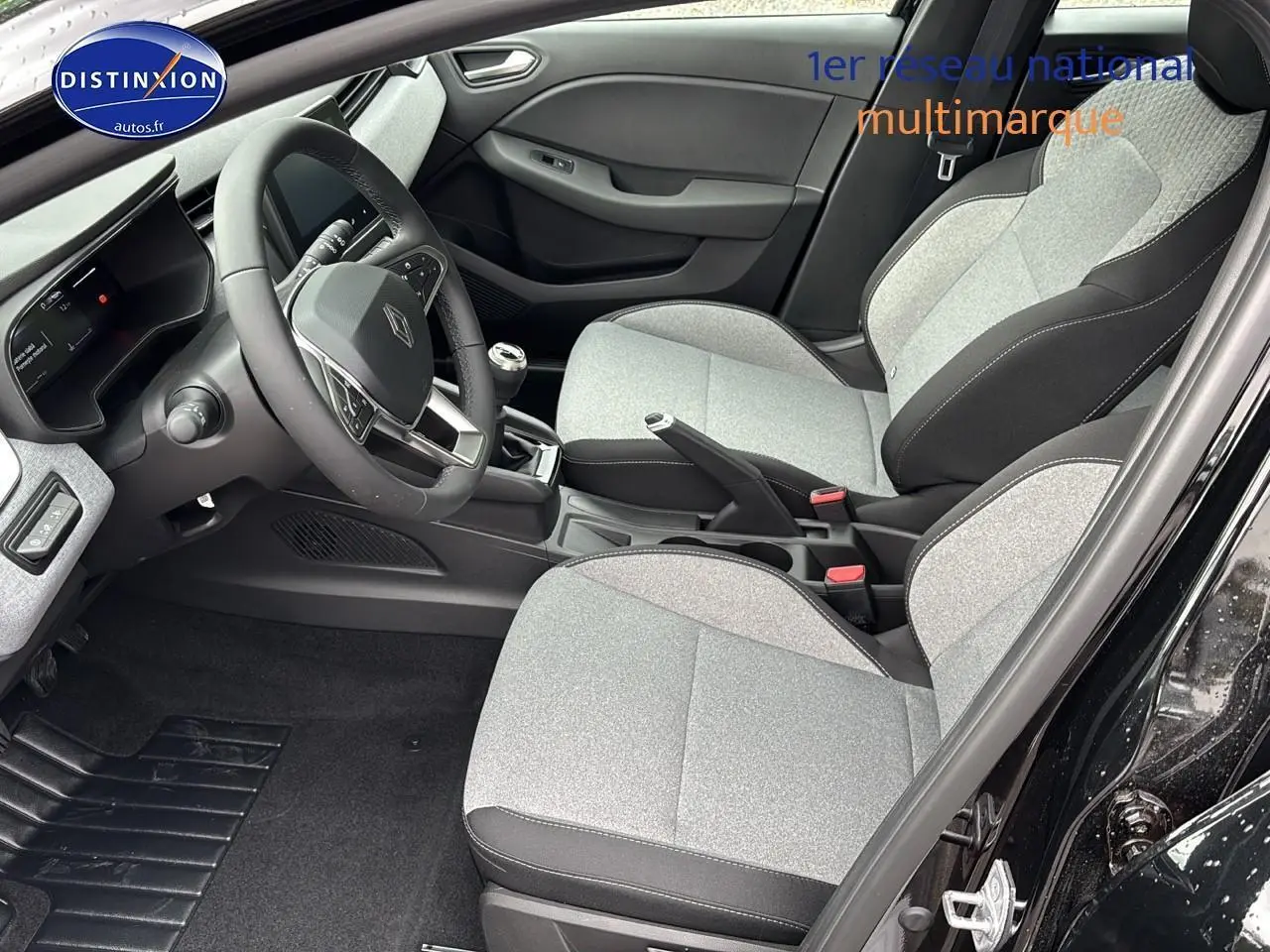 Intérieur avant droit de la Renault Clio V noire 2025 avec sièges gris clair et volant multifonction.