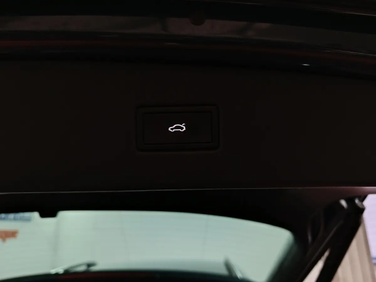 Bouton d'ouverture électrique du coffre visible sur le hayon intérieur d'un Volkswagen Tiguan bleu, vue arrière ouverte.