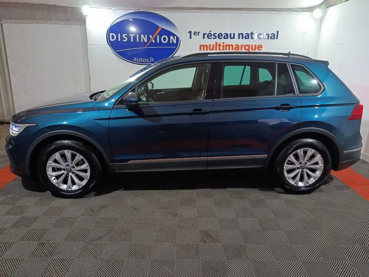 Vue latérale droite d'un Volkswagen Tiguan bleu 2021 garé en intérieur avec jantes alliage et toit noir.