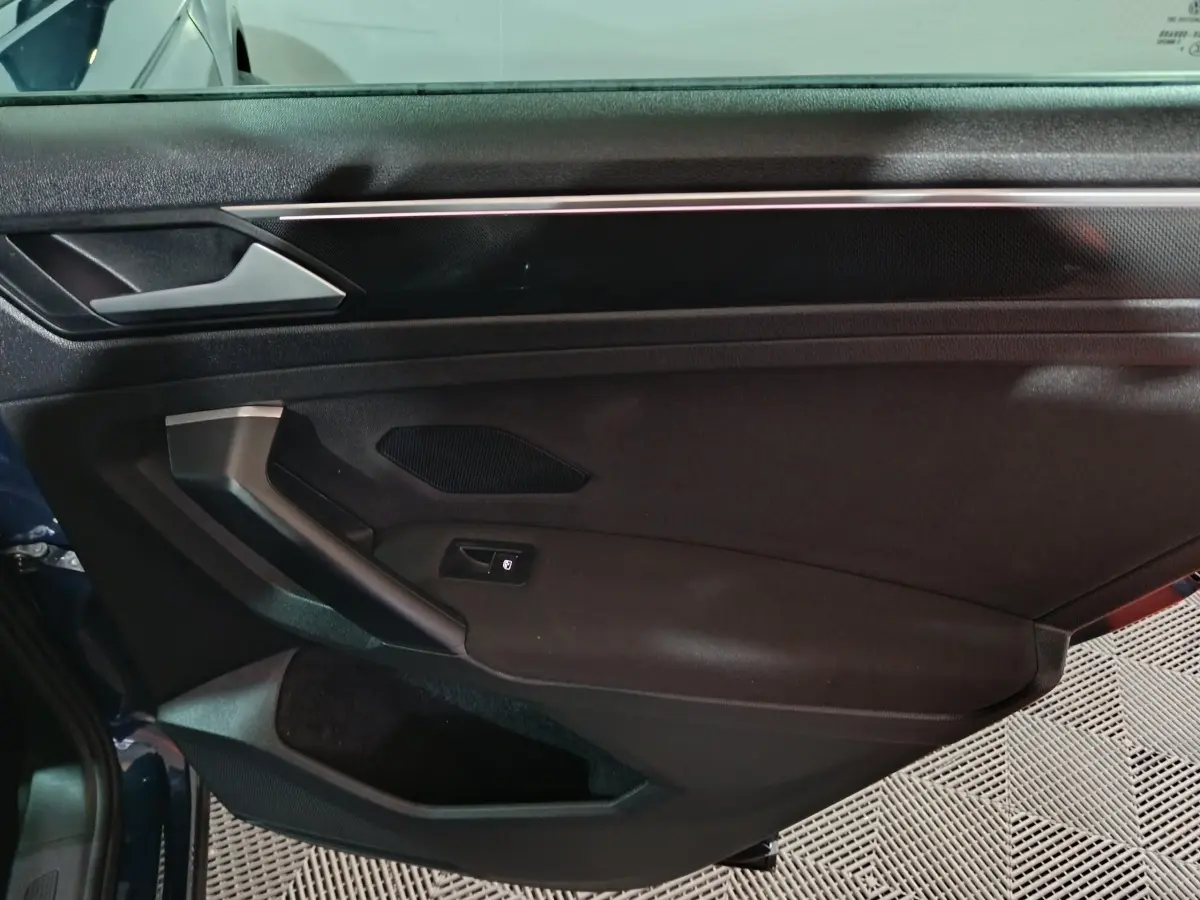 Vue intérieure côté gauche de la porte avant d’un Volkswagen Tiguan bleu, avec poignée et commande de vitre électrique.