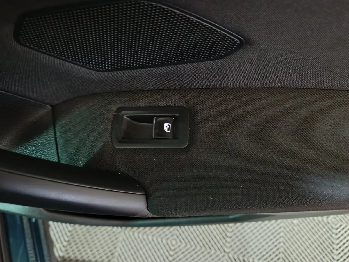 Vue rapprochée de la poignée intérieure et bouton de lève-vitre sur la porte côté conducteur du Volkswagen Tiguan bleu.