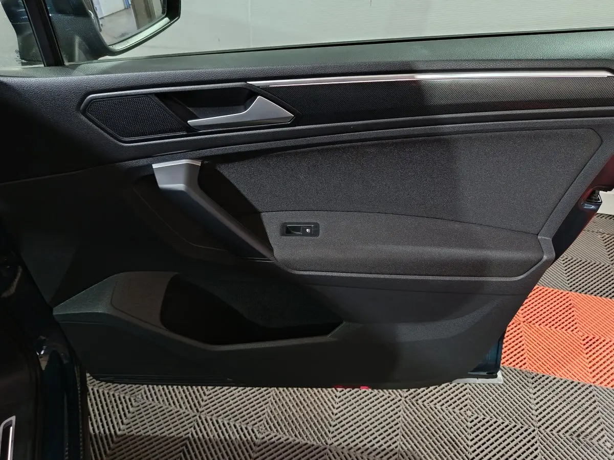 Vue intérieure de la porte avant gauche du Volkswagen Tiguan bleu, avec poignée argentée et panneau noir texturé.