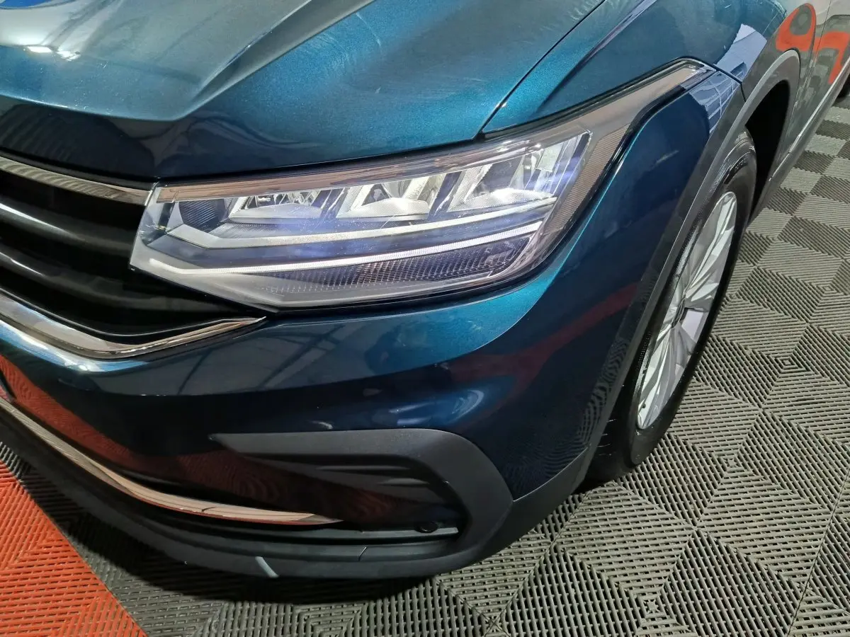 Gros plan sur l'avant droit bleu métallisé du Volkswagen Tiguan 1.5 TSI avec phares LED et calandre chromée.