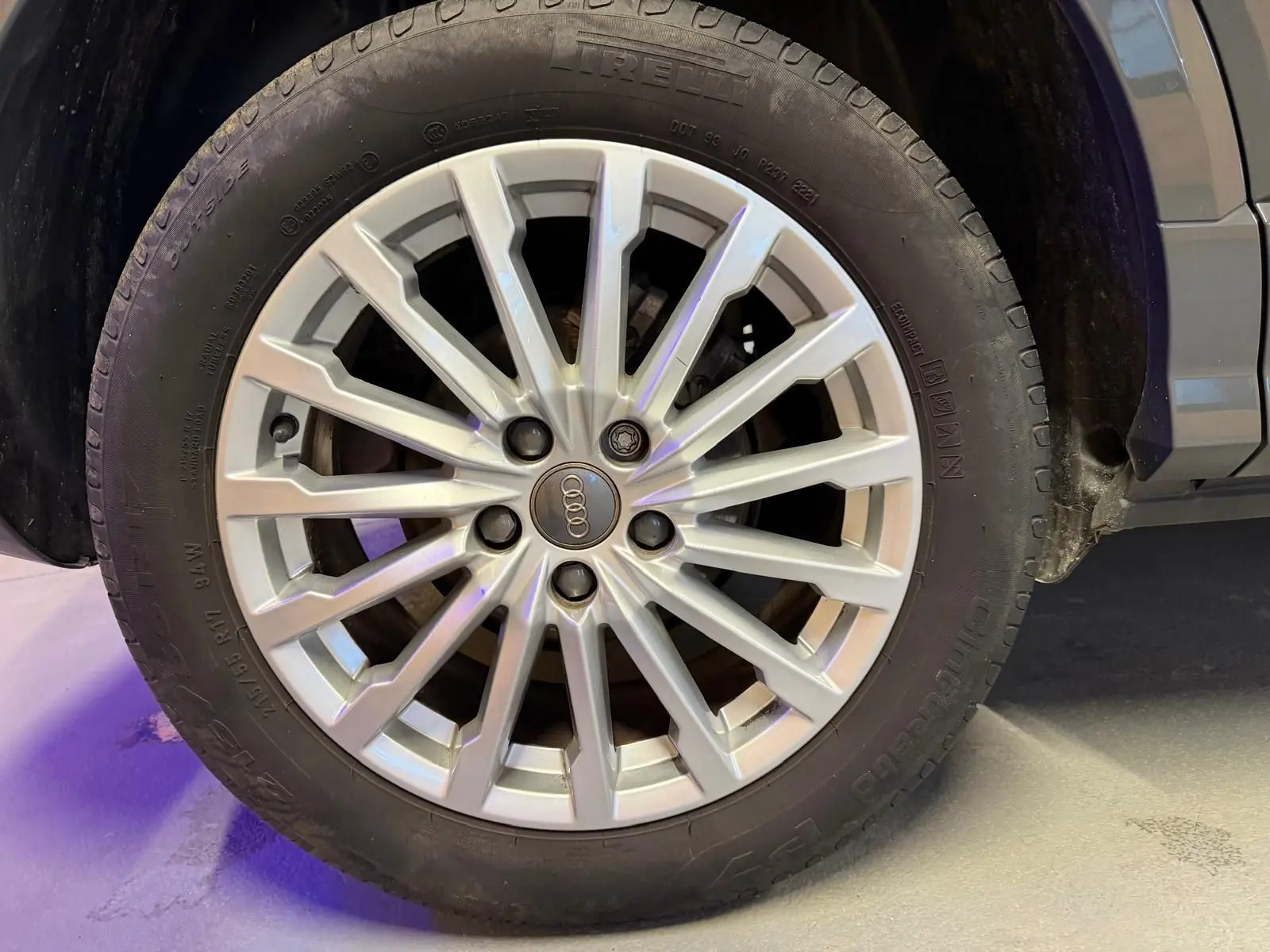 Gros plan sur la jante alu argentée de l'Audi Q2 gris, avec pneu Pirelli visible et partie de l'aile arrière.