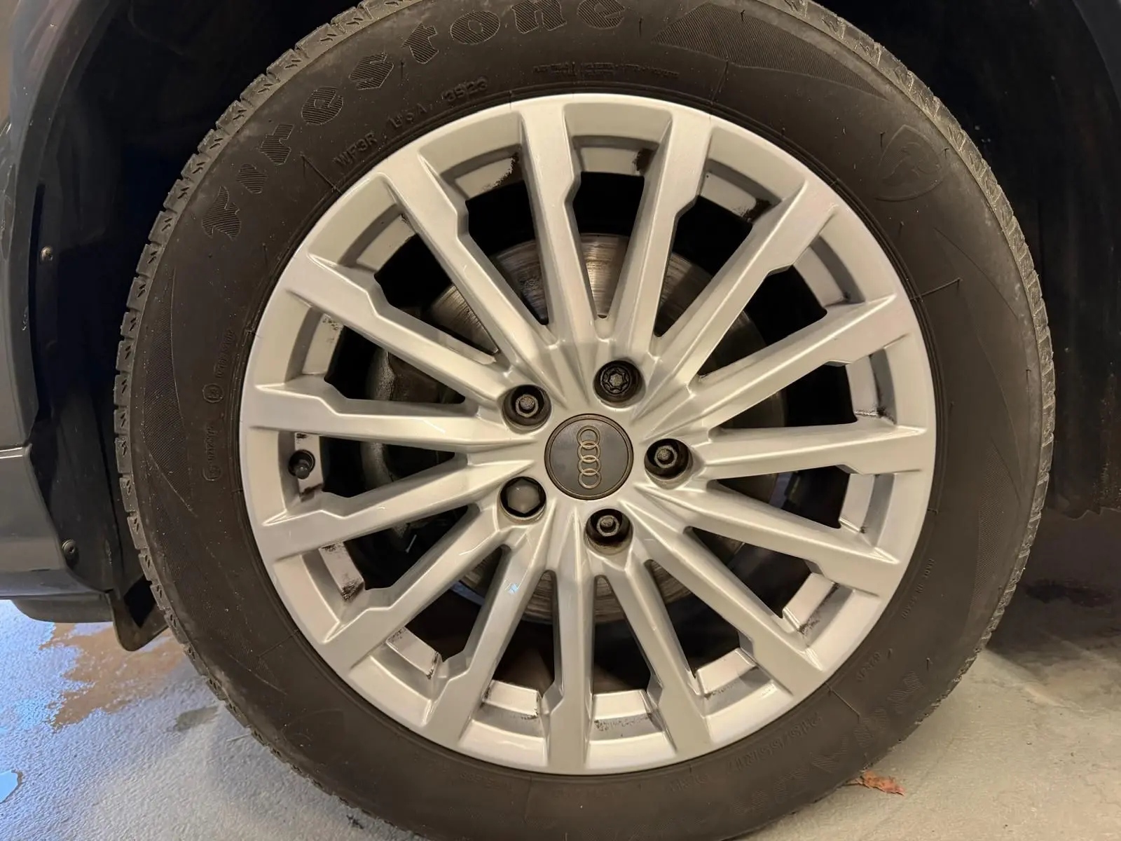 Gros plan sur la jante alu argentée d'un Audi Q2 gris, mettant en valeur le logo Audi au centre.