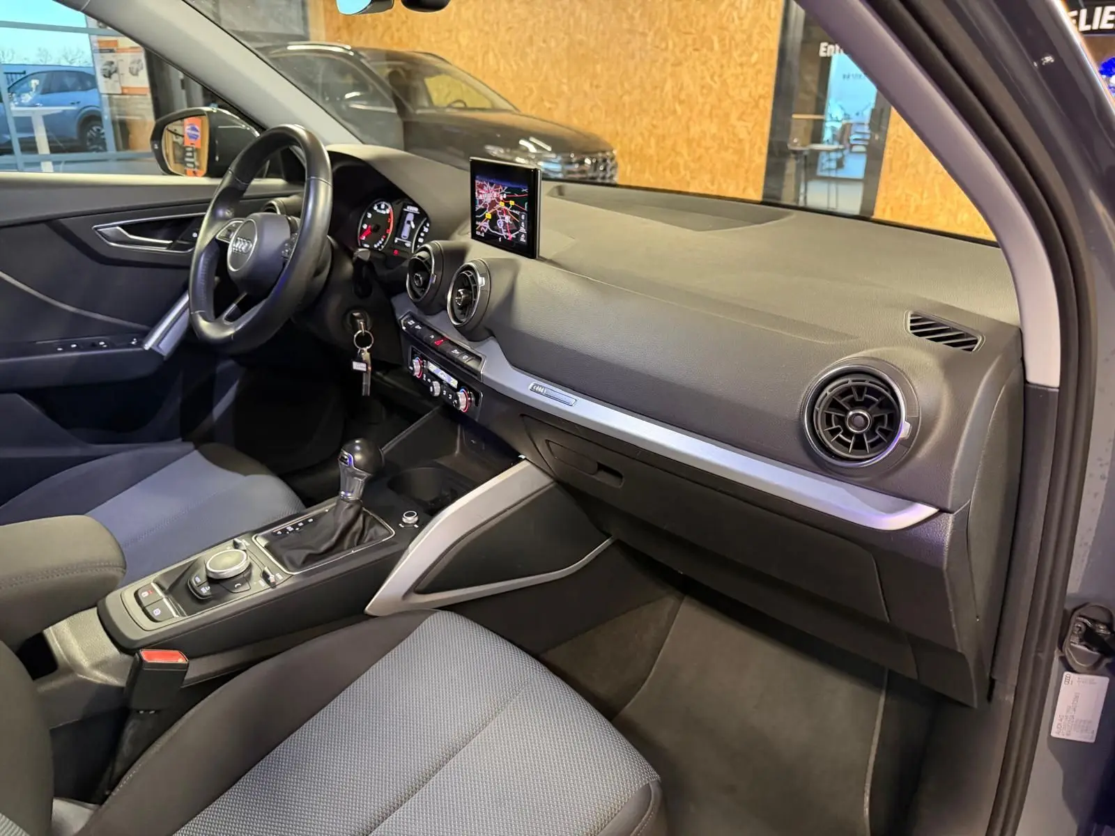 Vue intérieure côté passager de l'Audi Q2 gris, mettant en valeur le tableau de bord et la console centrale avec écran GPS.