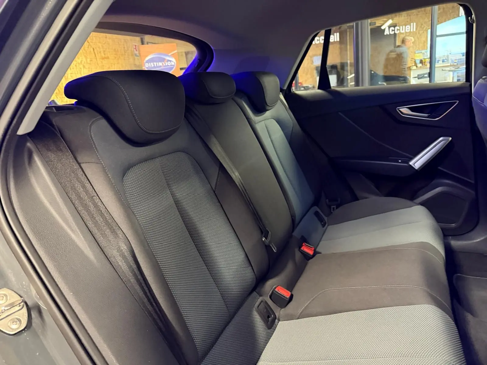 Vue intérieure côté droit montrant la banquette arrière gris foncé et clair de l'Audi Q2 avec appuie-têtes et ceintures de sécurité.