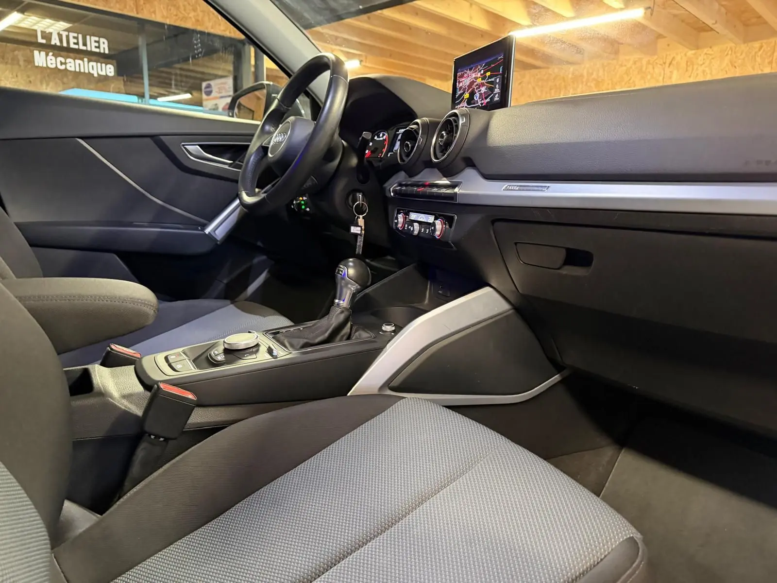 Intérieur Audi Q2 gris vu côté passager, tableau de bord avec écran GPS et console centrale avec levier de vitesse.
