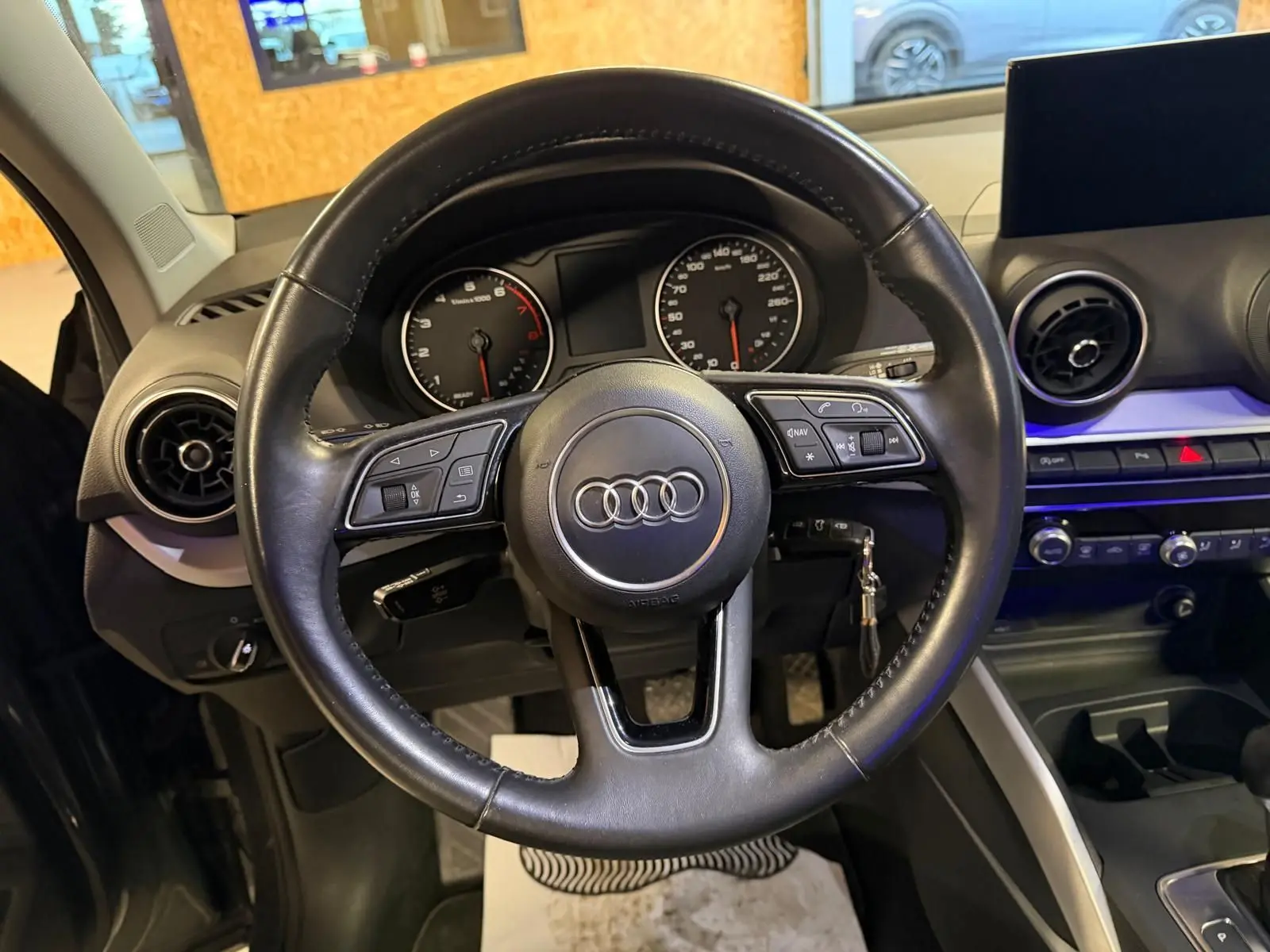 Vue intérieure centrée sur le volant cuir multifonctions noir de l'Audi Q2 avec tableau de bord et écran multifonction.