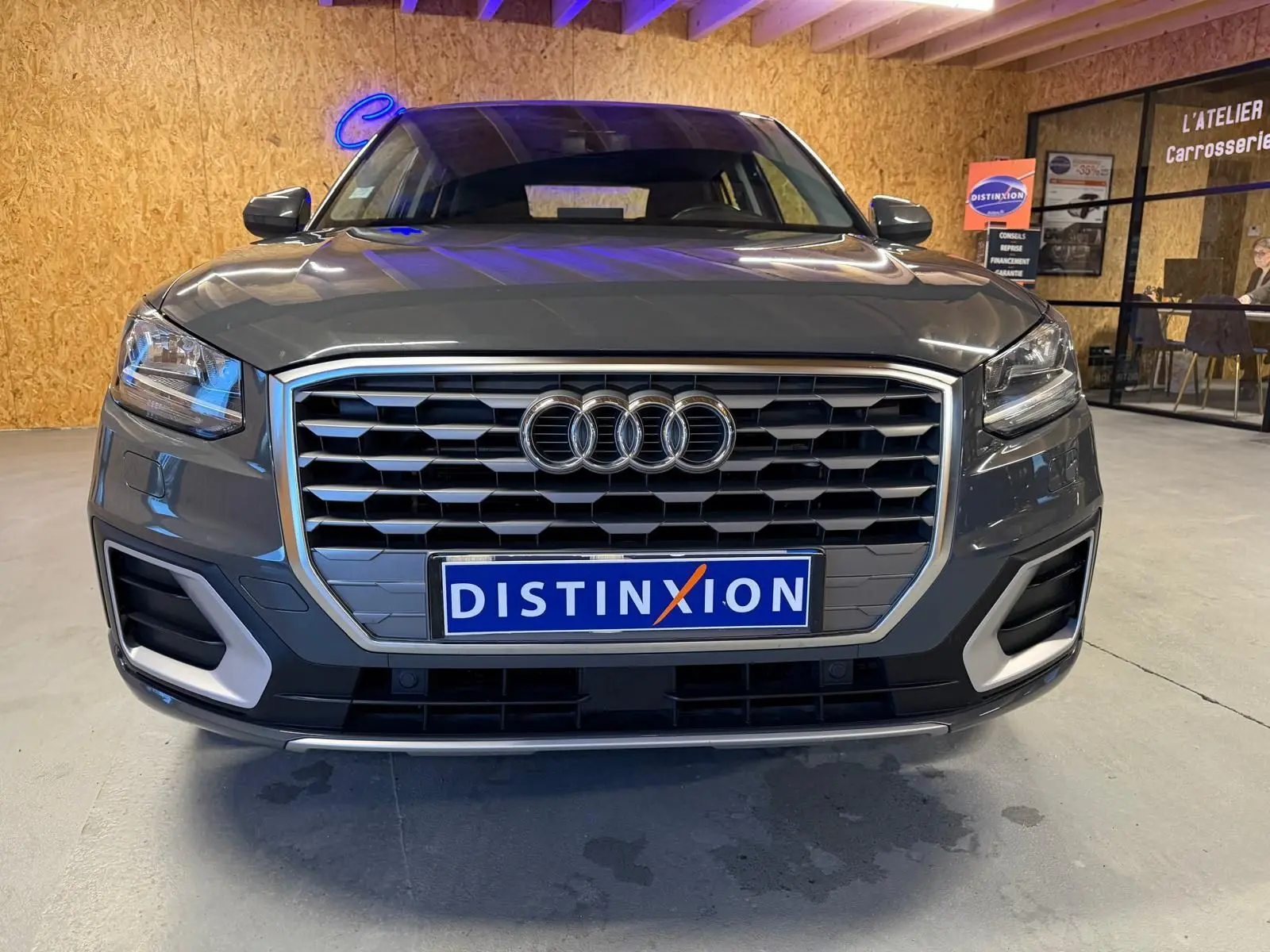 Vue frontale d'un Audi Q2 gris avec calandre hexagonale et détails chromés, en intérieur d'atelier.