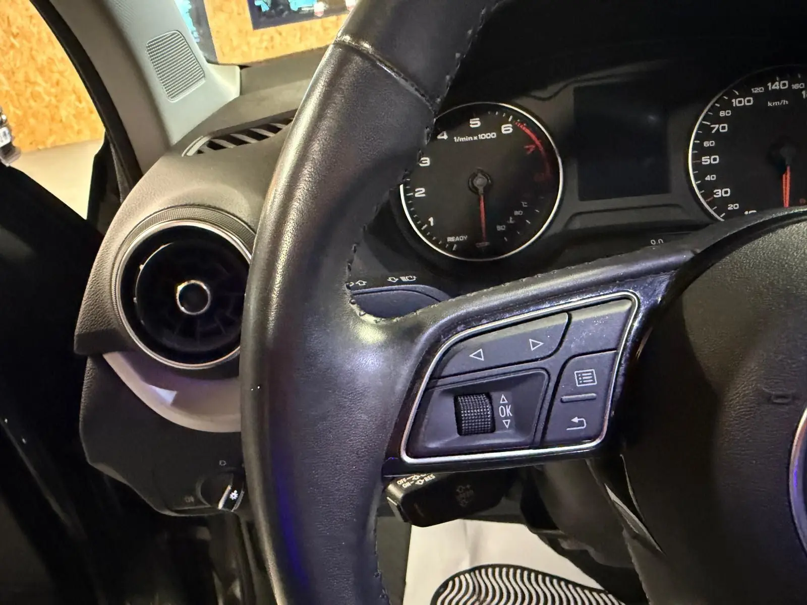 Gros plan sur le volant cuir et le tableau de bord noir de l'Audi Q2, avec commandes multifonctions visibles.