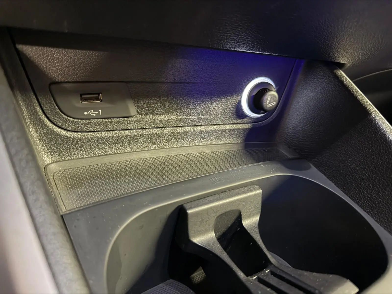 Gros plan sur la prise USB et l’allume-cigare dans l’espace de rangement noir de l’Audi Q2 gris.