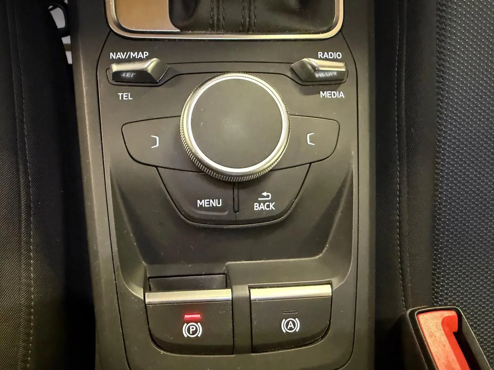 Vue rapprochée de la console centrale noire de l'Audi Q2 avec molette de contrôle et boutons de frein à main et auto-hold.