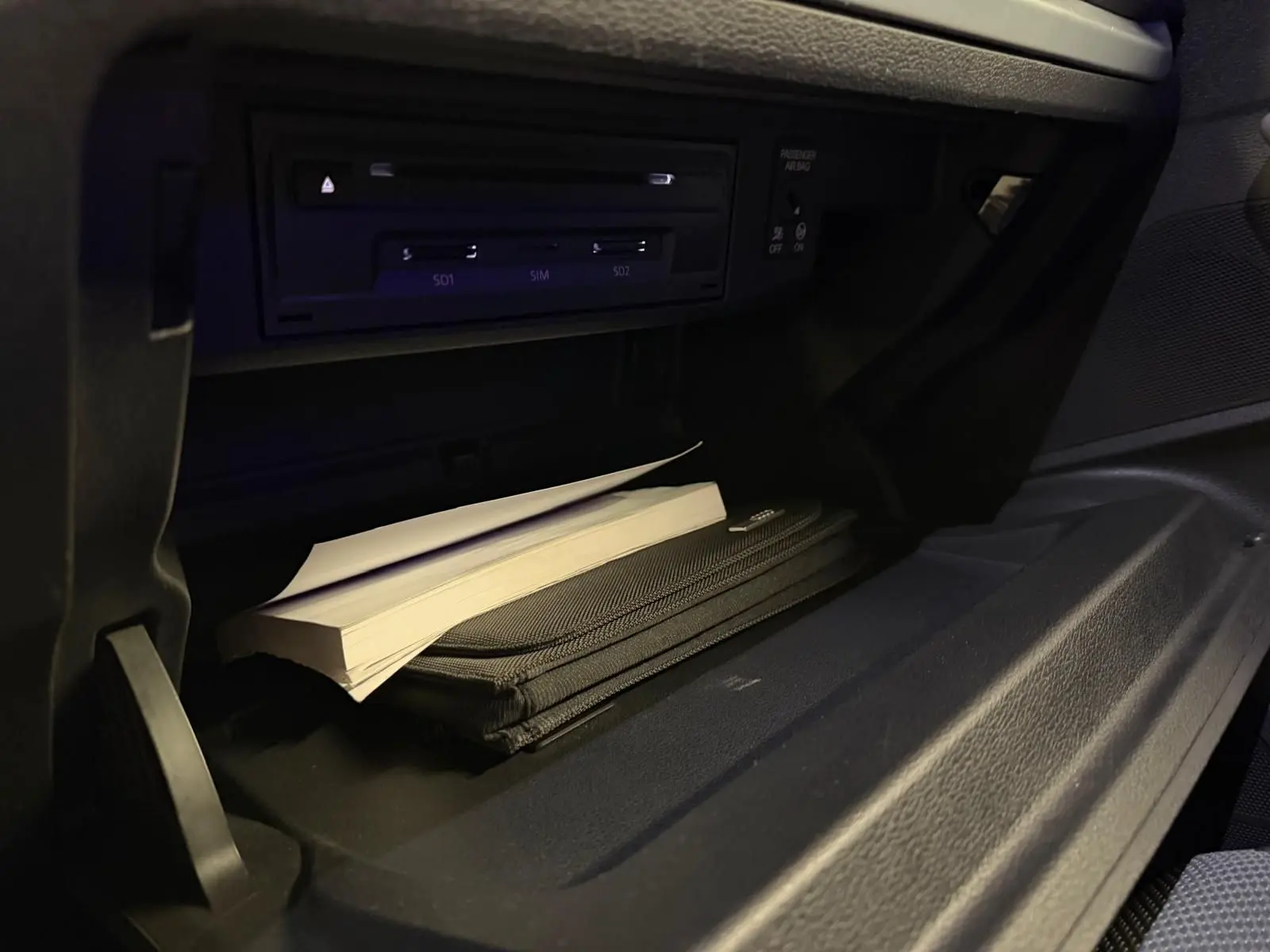 Gros plan sur la boîte à gants ouverte de l'Audi Q2 gris, montrant un manuel et un étui de rangement.