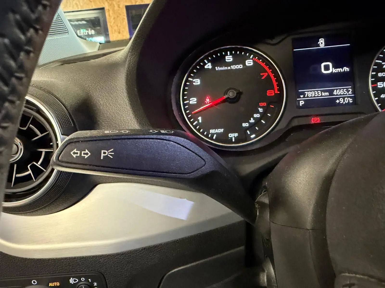 Gros plan sur le commodo gauche du tableau de bord de l'Audi Q2 gris, avec compte-tours et écran multifonction en arrière-plan.