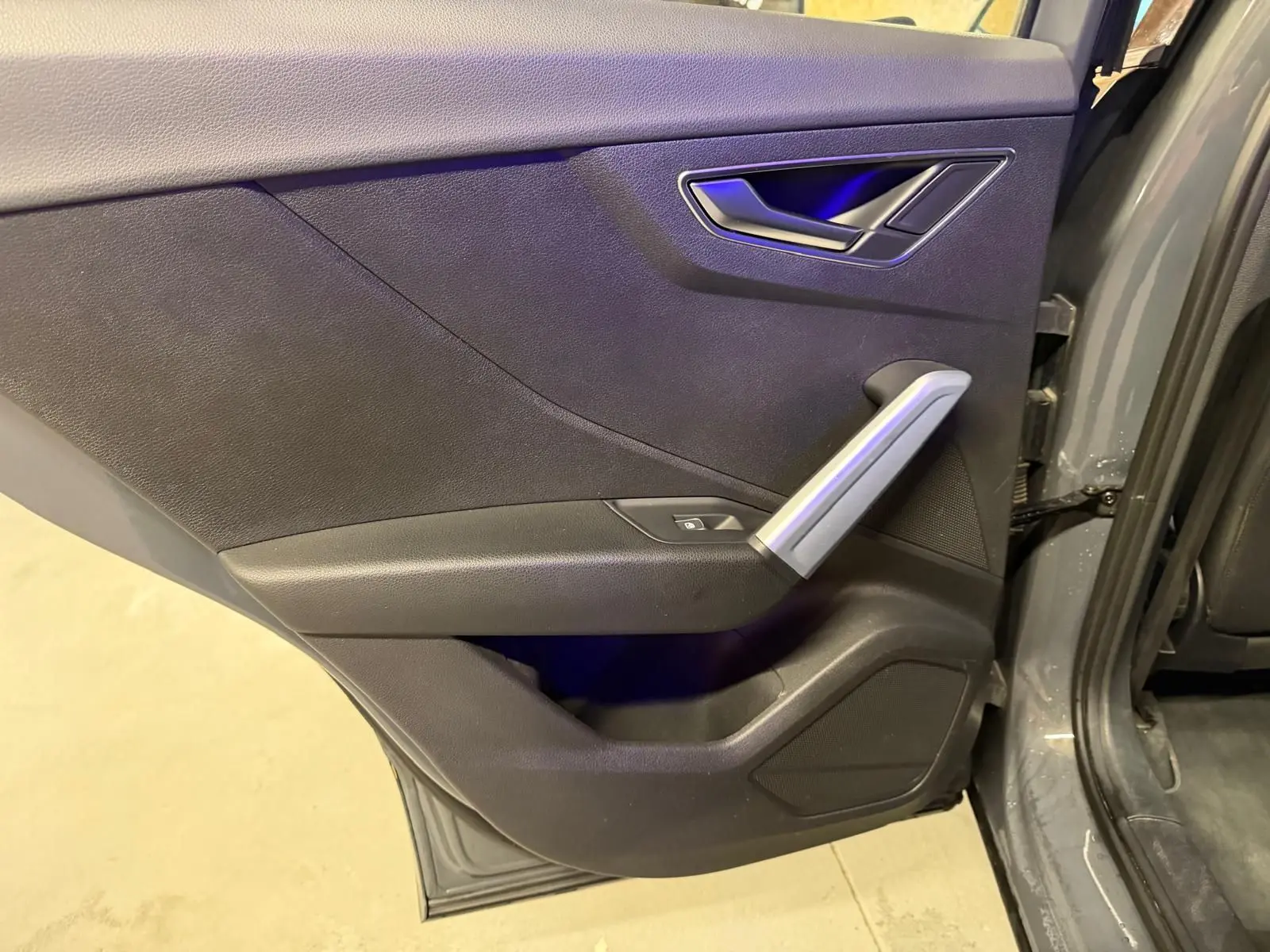 Vue rapprochée de la porte arrière droite gris foncé de l'Audi Q2 avec poignée argentée et bouton de vitre électrique.