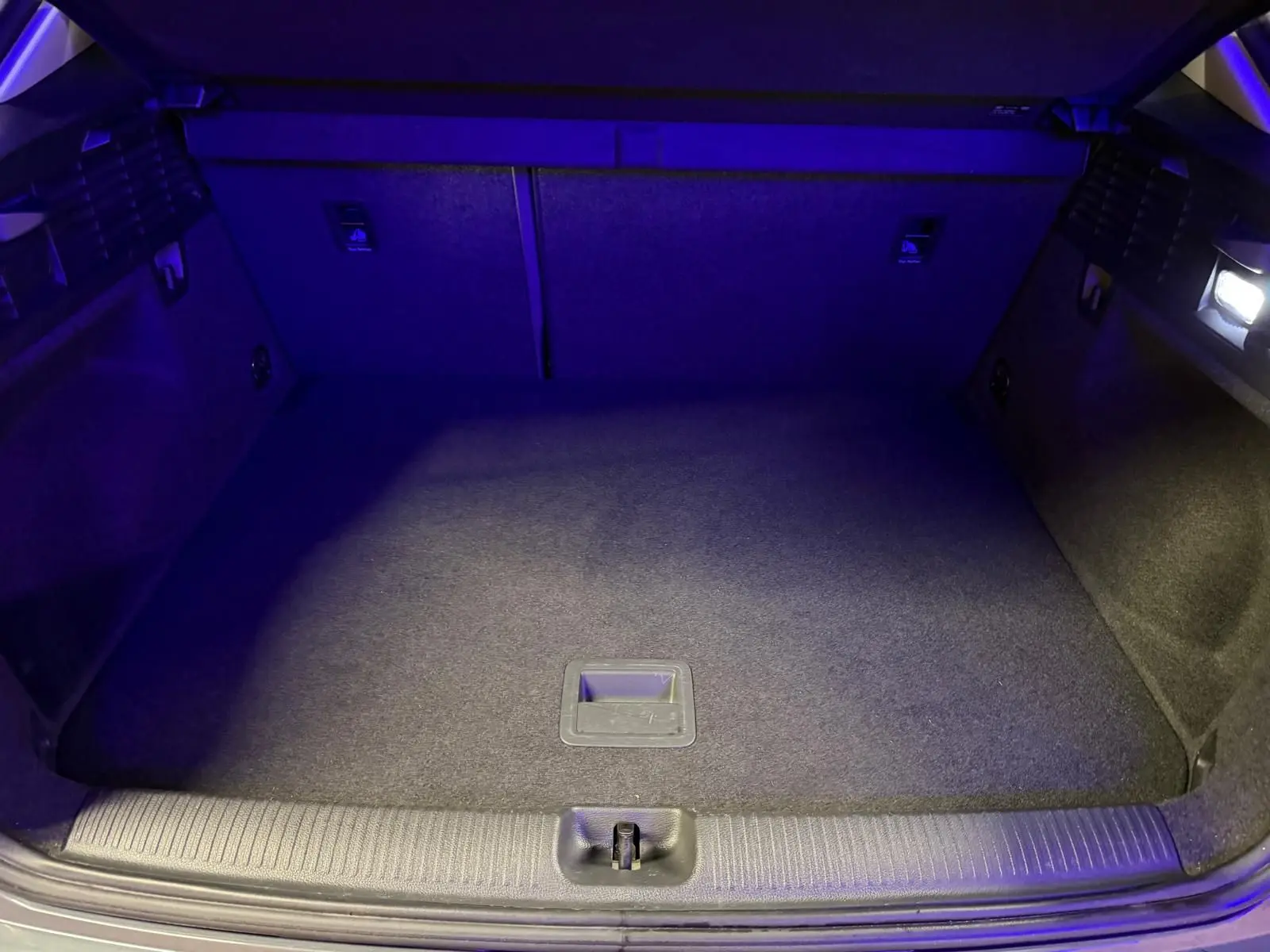 Coffre ouvert de l'Audi Q2 gris, vue intérieure montrant le tapis de sol et l'éclairage latéral droit.