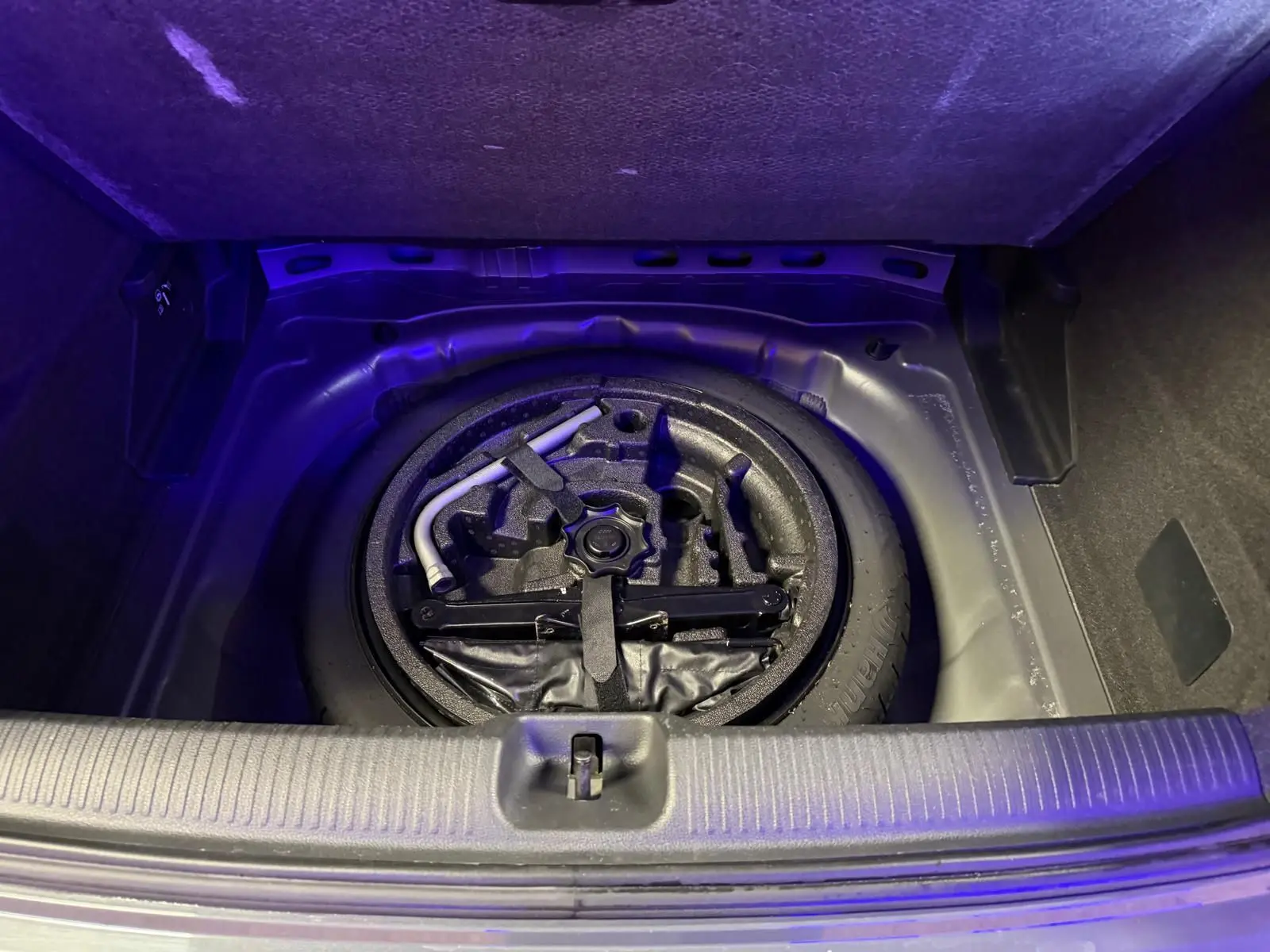 Vue plongeante sur la roue de secours et les outils dans le coffre d'un Audi Q2 gris 2018.