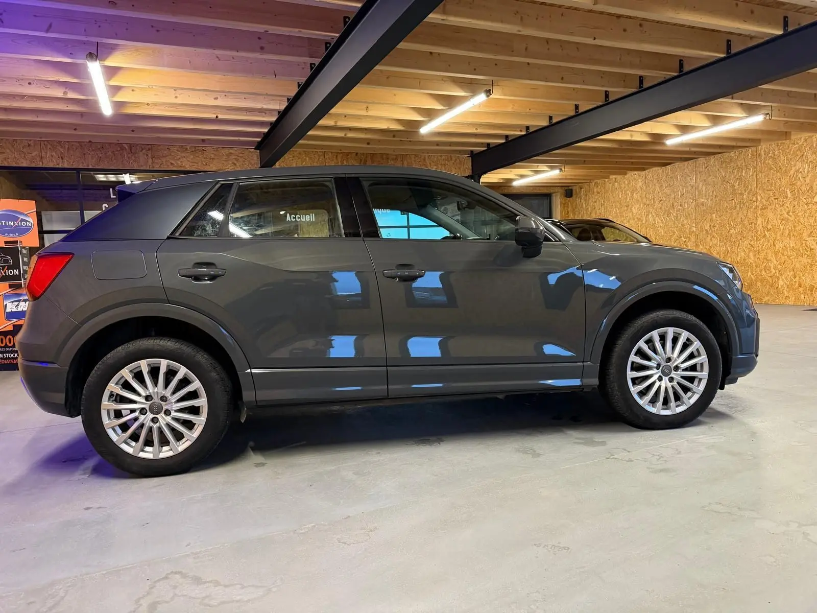 Audi Q2 gris vue de profil côté gauche dans un garage, avec jantes alliage et rétroviseurs noirs.