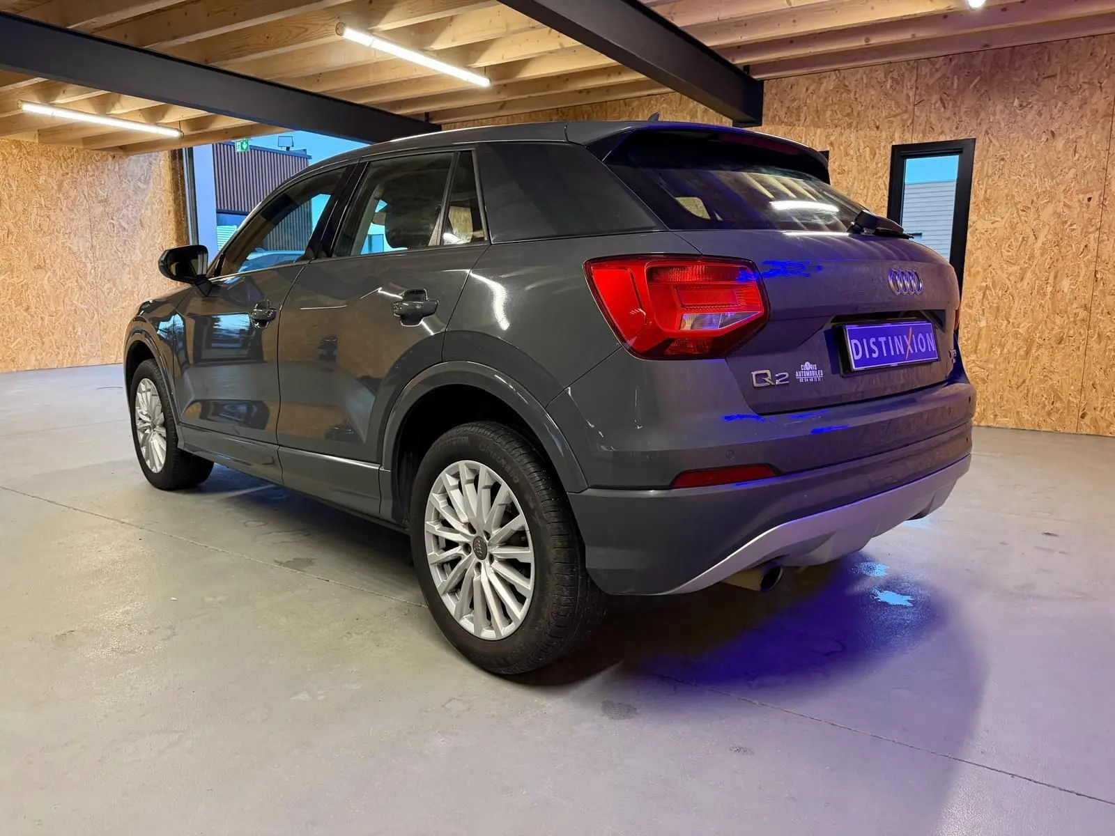 Audi Q2 gris vue 3/4 arrière droit en intérieur, avec jantes alu et sorties d'échappement chromées visibles.