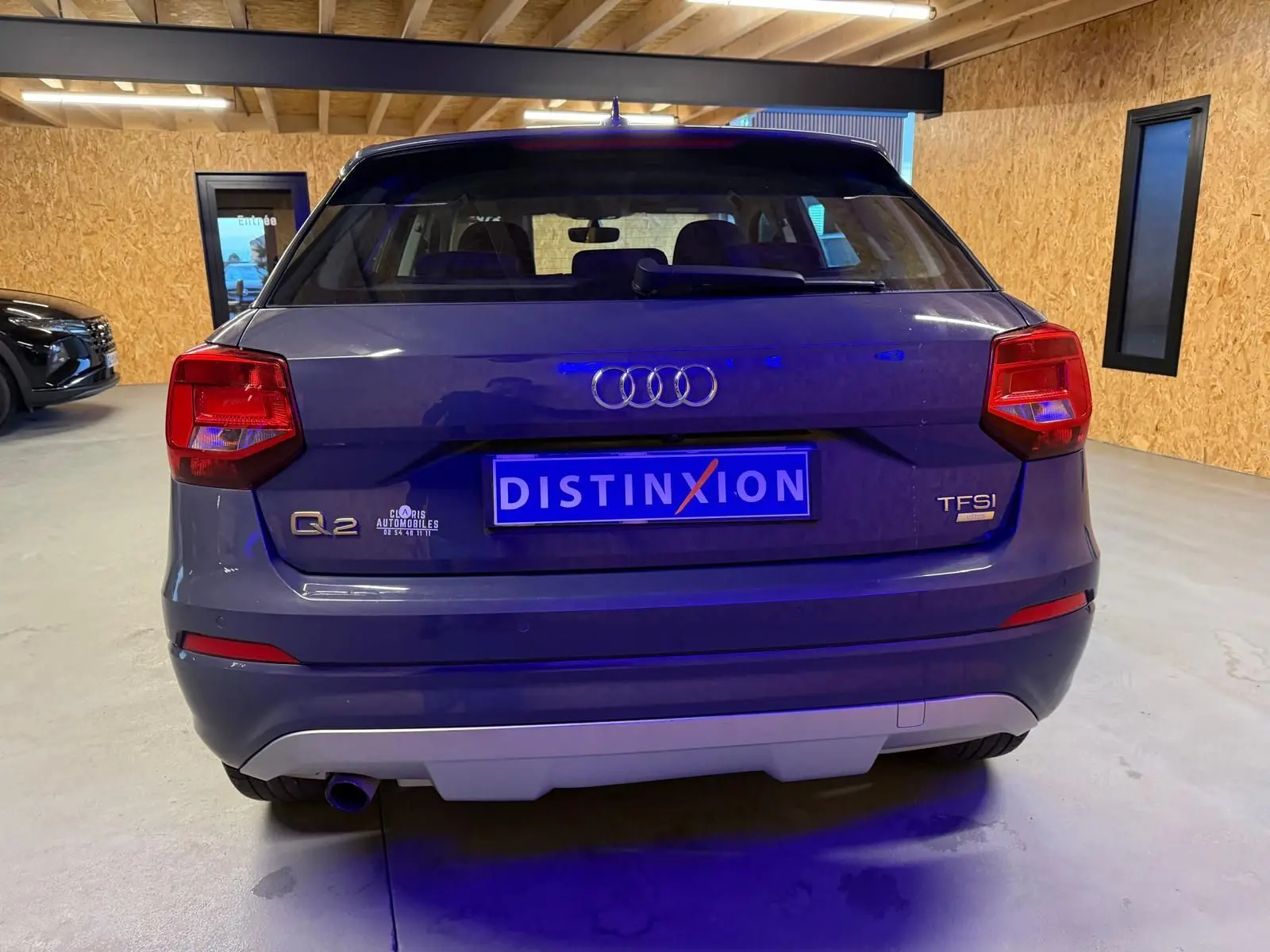 Vue arrière d'un Audi Q2 gris avec feux rouges, logo TFSI et plaque Distinxion dans un garage.