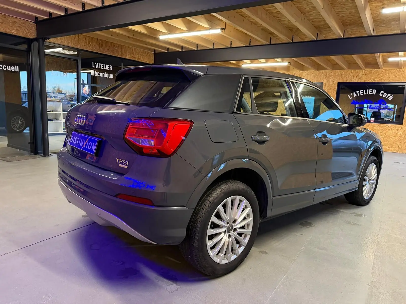Audi Q2 gris vue 3/4 arrière droit en intérieur, avec jantes alu et feux arrière LED visibles.