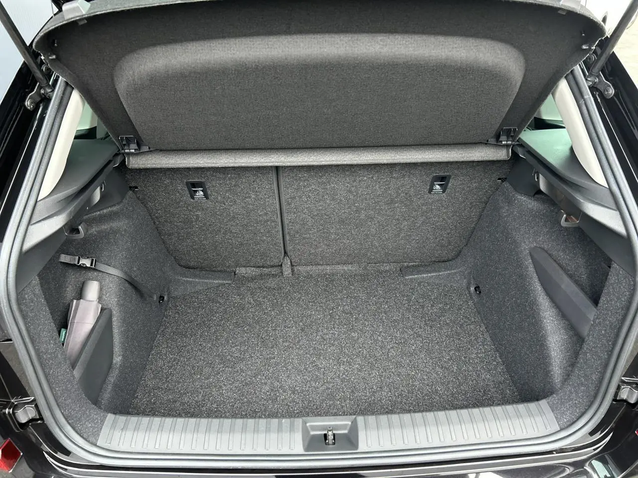 Coffre ouvert vu de l'arrière d'un Skoda Kamiq noir Magic, intérieur gris et compartiments latéraux visibles.