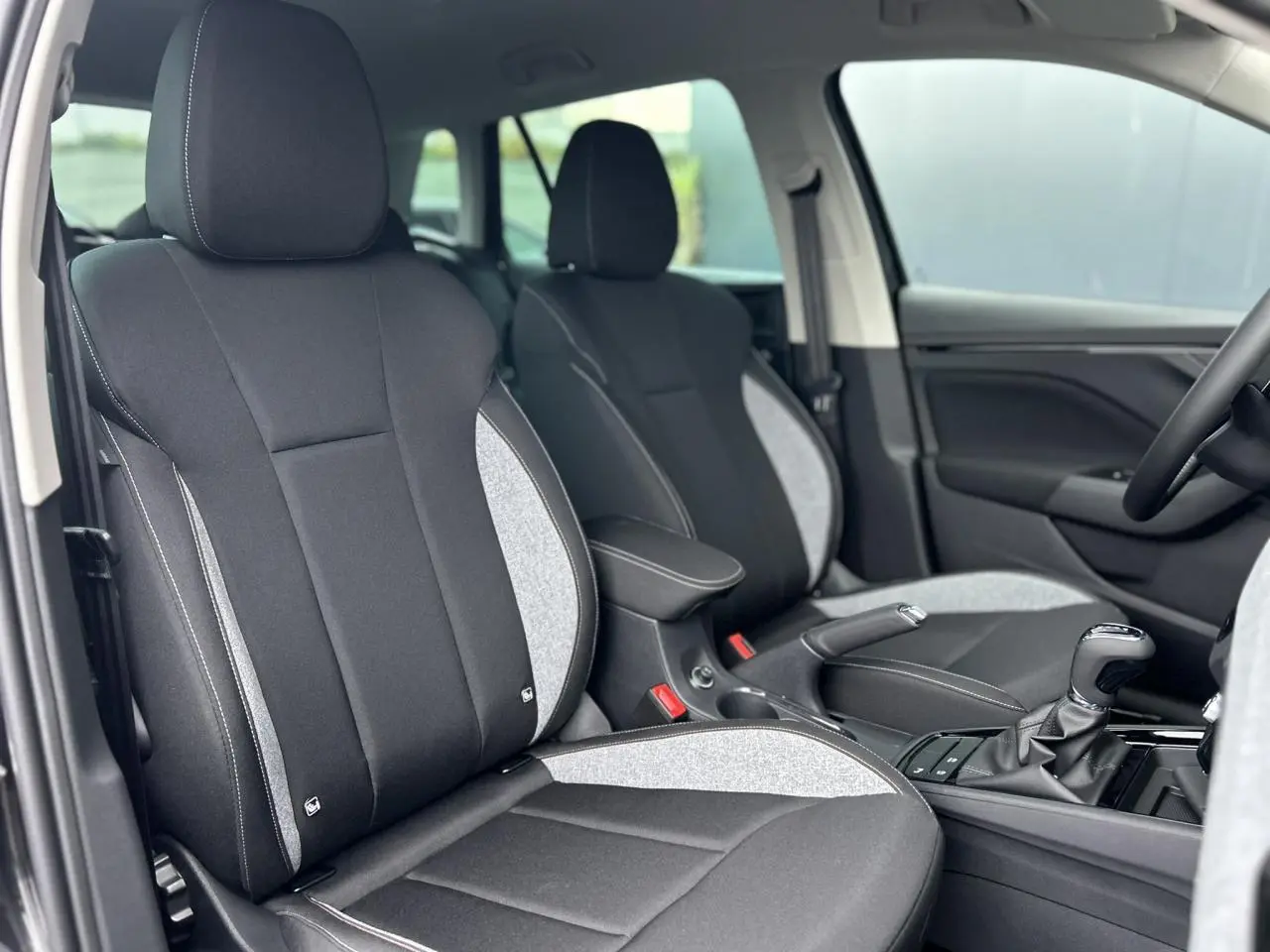 Vue intérieure rapprochée des sièges avant noirs et gris du Skoda Kamiq 2025 avec console centrale et levier de vitesse.