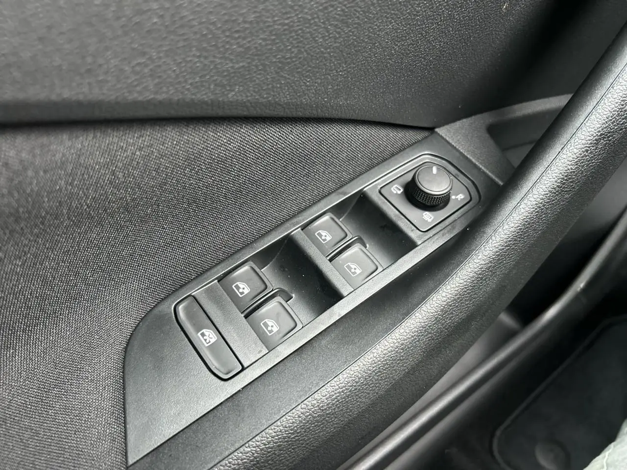 Gros plan sur les commandes de lève-vitres et réglage des rétroviseurs côté conducteur d’un Skoda Kamiq noir Magic.