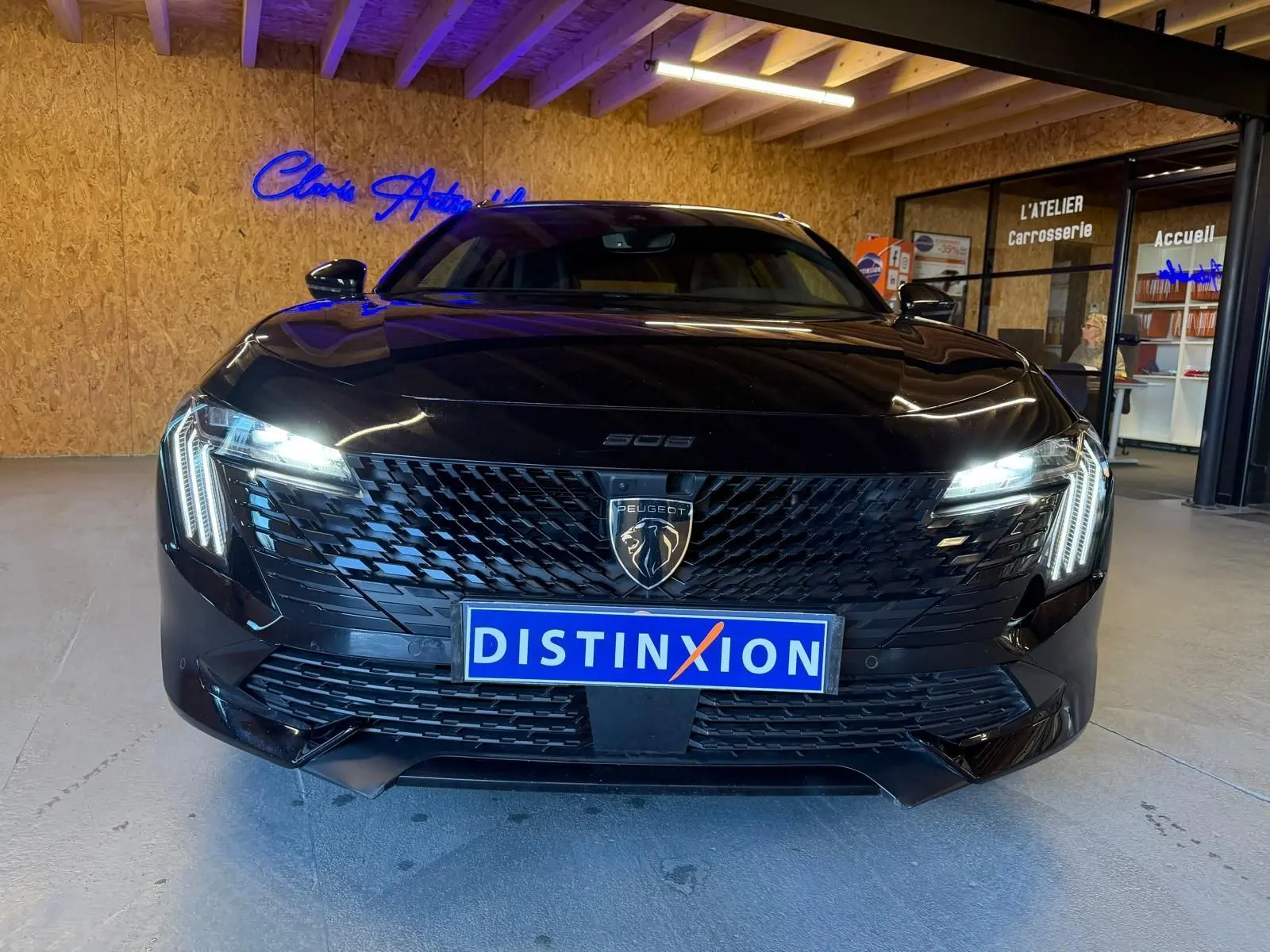 Vue frontale d'une Peugeot 508 SW noire avec calandre noire brillante et feux LED allumés en intérieur showroom.