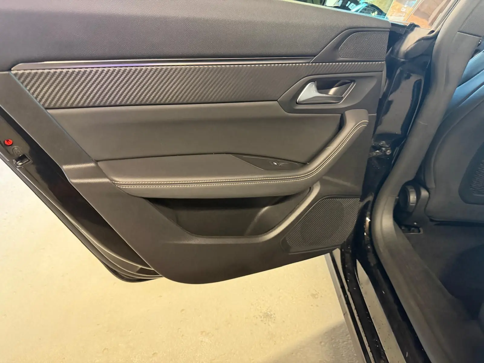 Vue intérieure du panneau de porte arrière gauche noir avec surpiqûres et insert effet carbone d'une Peugeot 508 SW 2024.