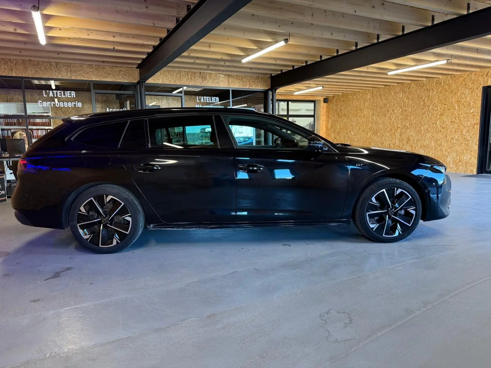 Peugeot 508 SW noir vue de profil côté gauche, avec jantes alliage 18'' bi-ton et badge GT visible sur l'aile avant.