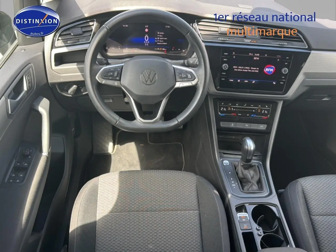 Vue intérieure avant du Volkswagen Touran noir 2025, volant cuir multifonction et écran tactile central visible.