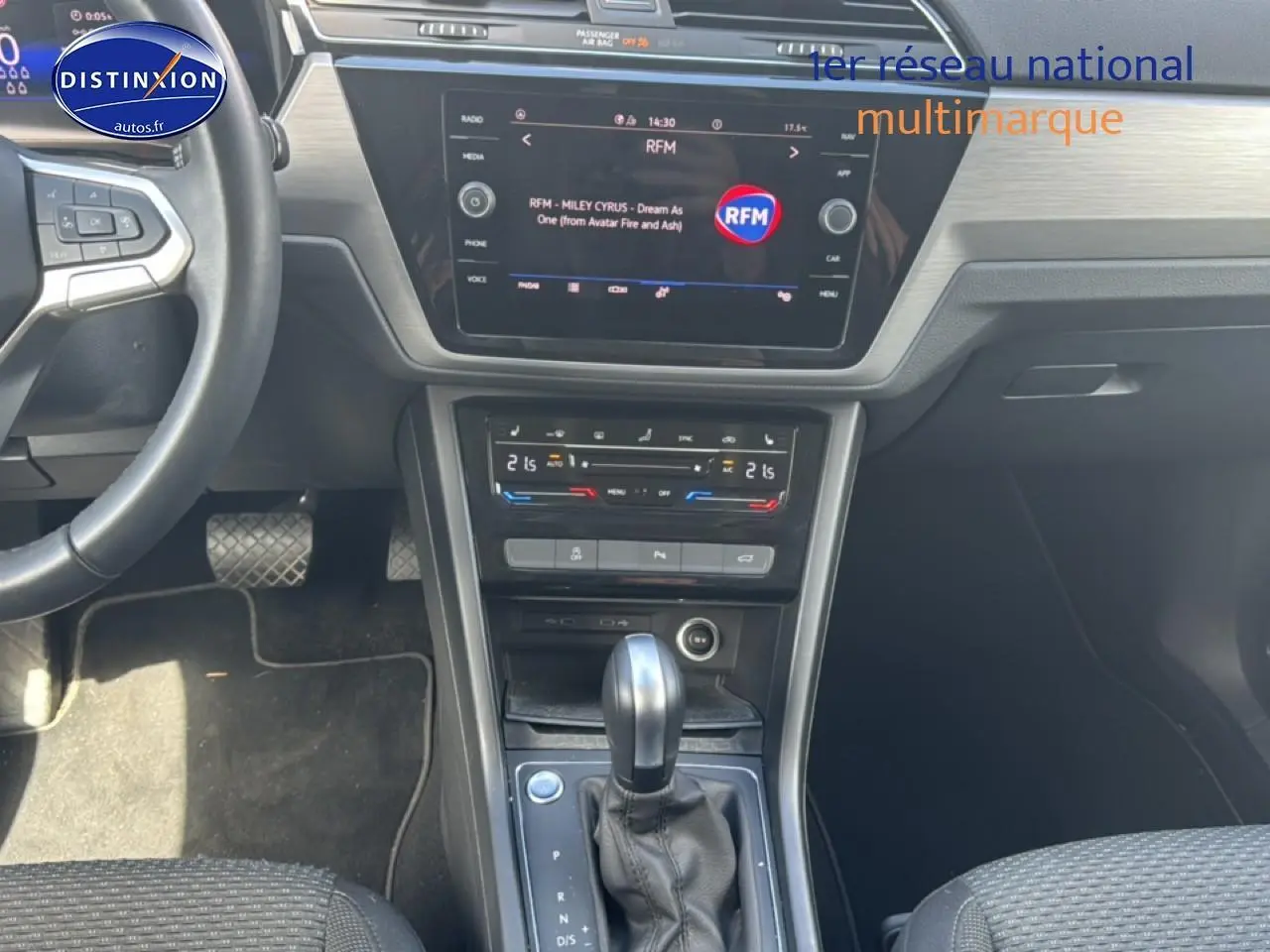 Vue intérieure centrée sur la console centrale et levier de vitesse d’un Volkswagen Touran noir, avec écran tactile et climatisation tri-zone.